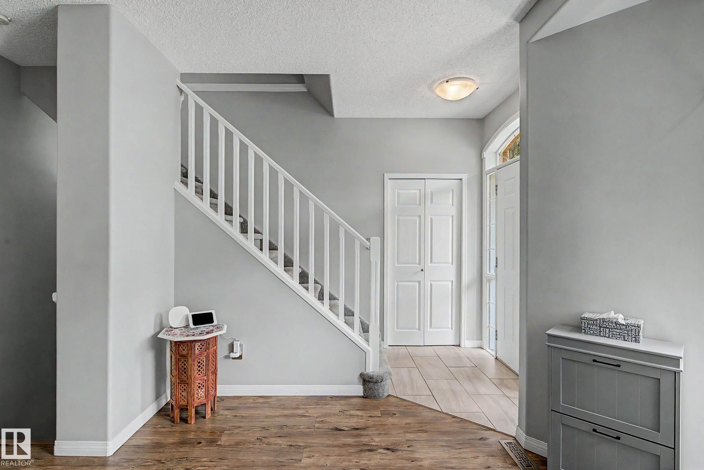 Foyer showcasing a wood-finish flooring, staircase with white railing, and a front entry door with an arched transom window - 9130 100A Avenue Nw, Edmonton, AB - Indoor Photo Showing Other Room