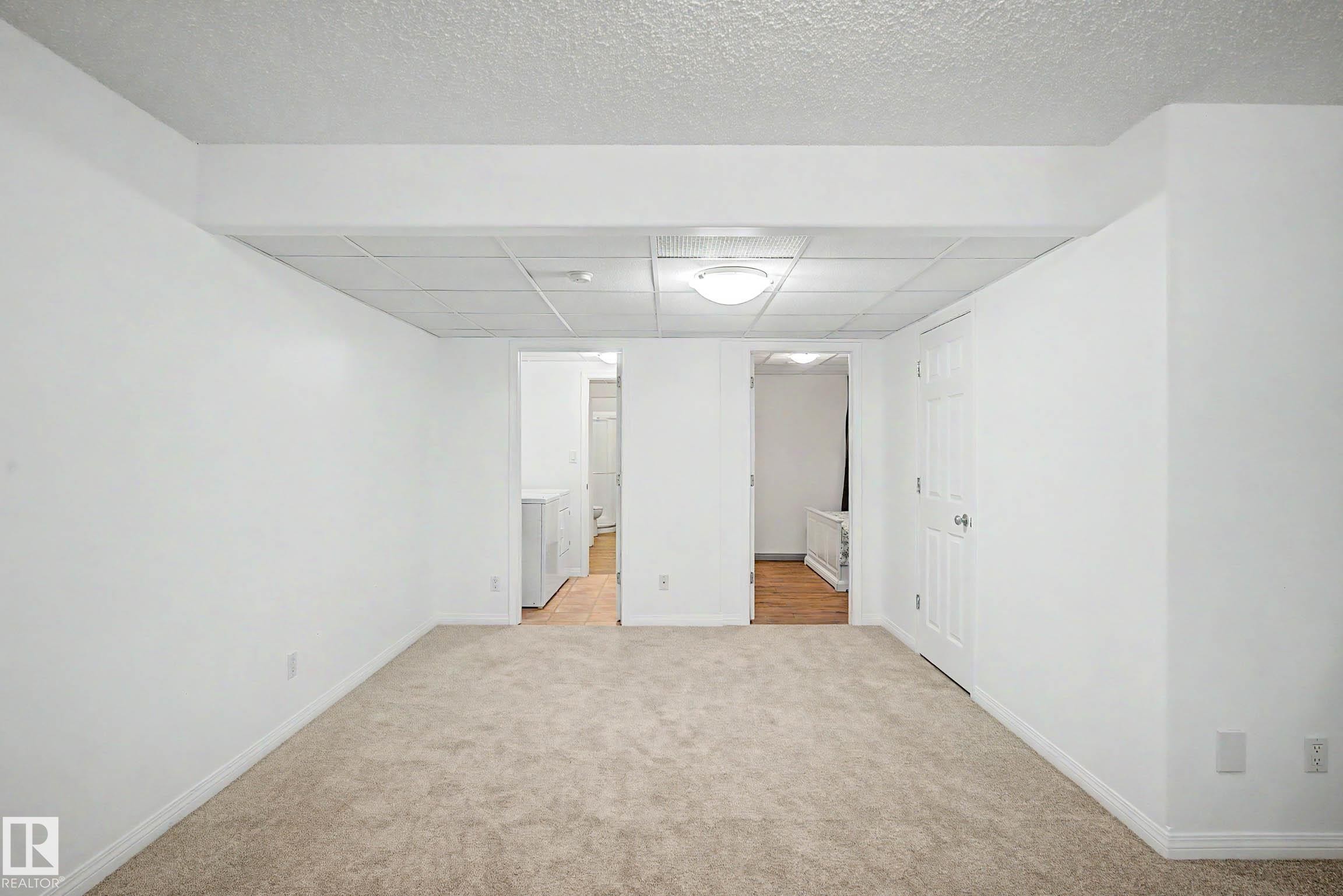 Spacious room featuring neutral carpeting, white walls, and a drop ceiling with integrated lighting - 9130 100A Avenue Nw, Edmonton, AB - Indoor Photo Showing Other Room