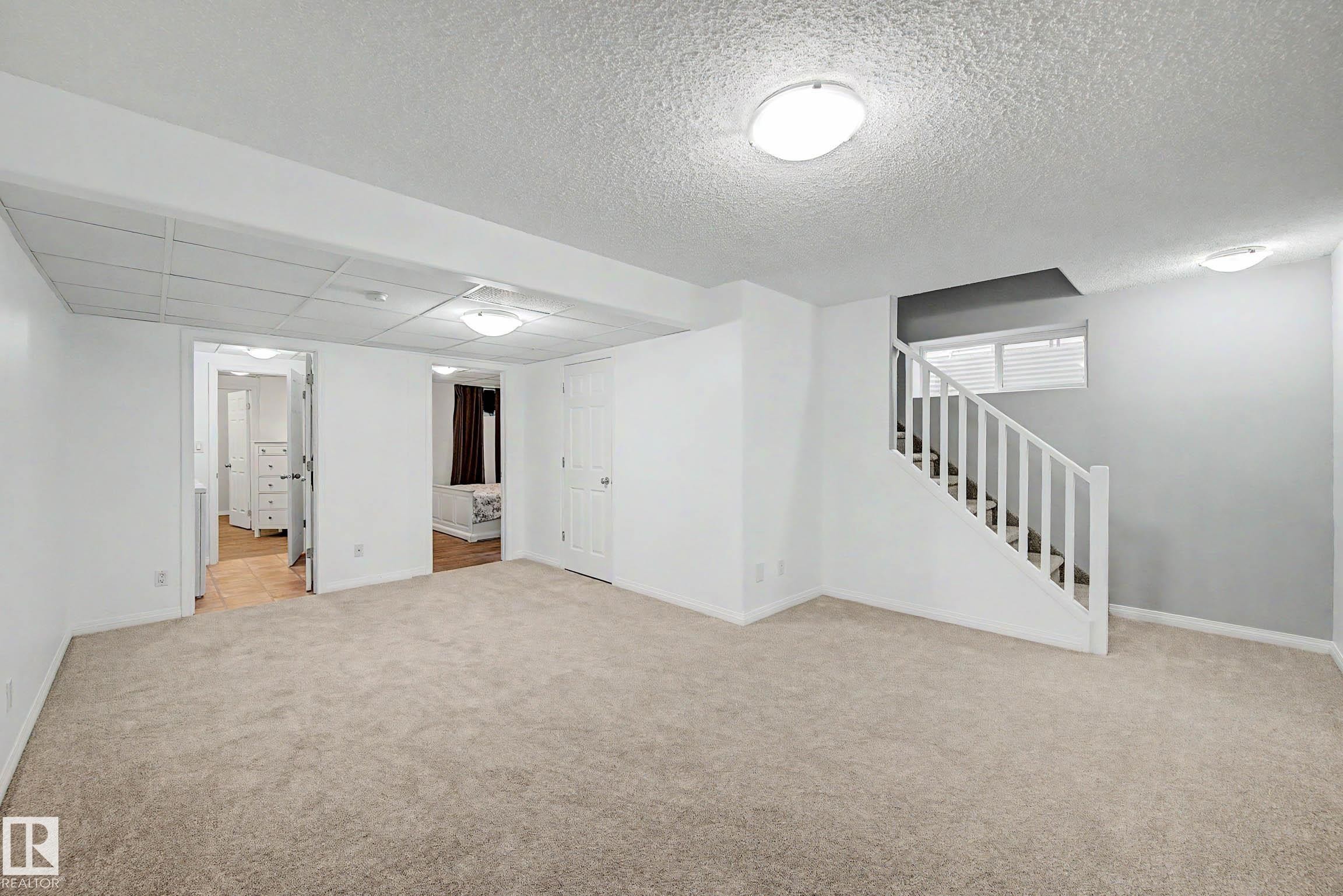 Carpeted room with a full staircase featuring white railings and a single window - 9130 100A Avenue Nw, Edmonton, AB - Indoor Photo Showing Other Room