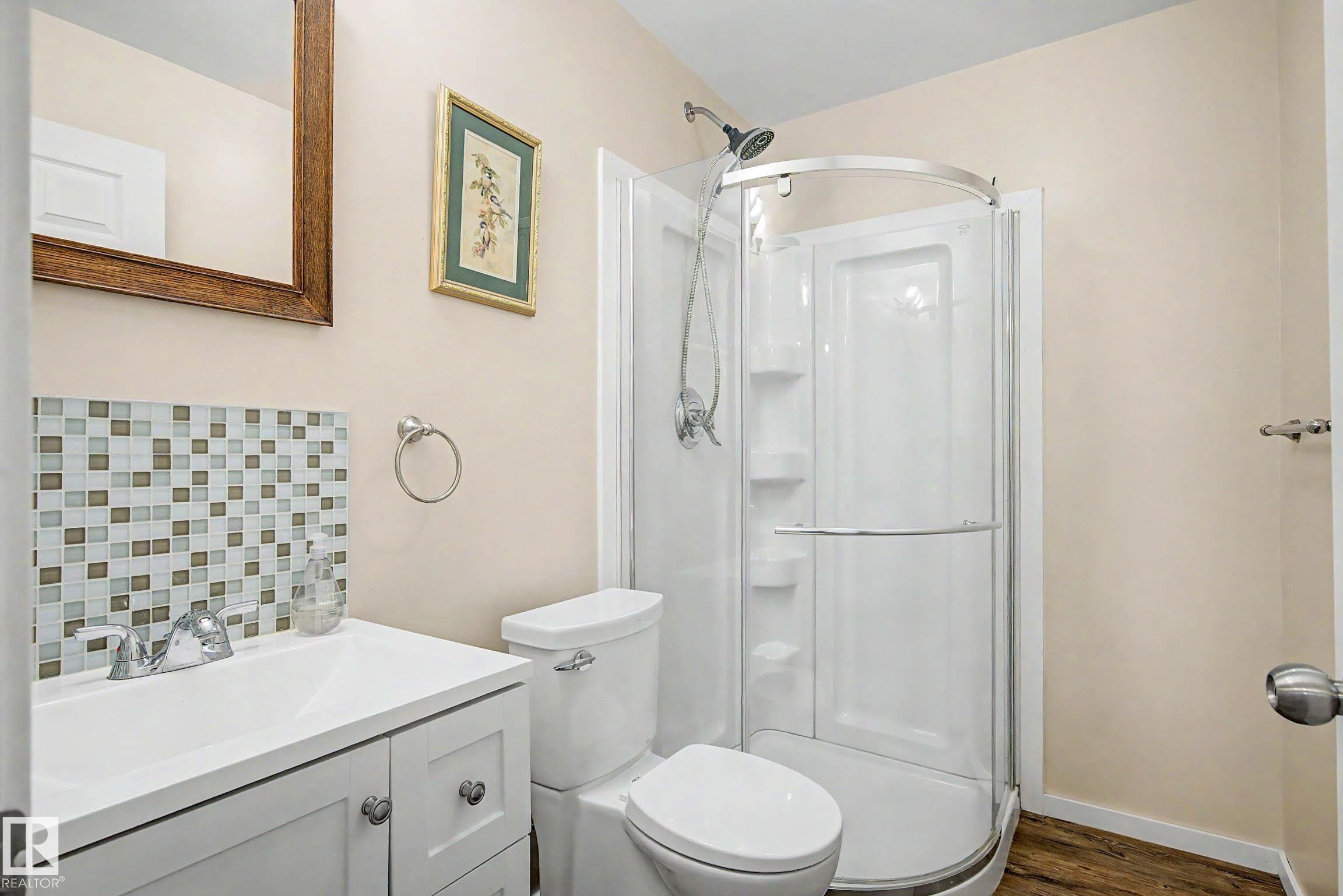 Compact bathroom featuring a white vanity with integrated sink, mosaic tile backsplash, and a corner shower enclosure - 9130 100A Avenue Nw, Edmonton, AB - Indoor Photo Showing Bathroom