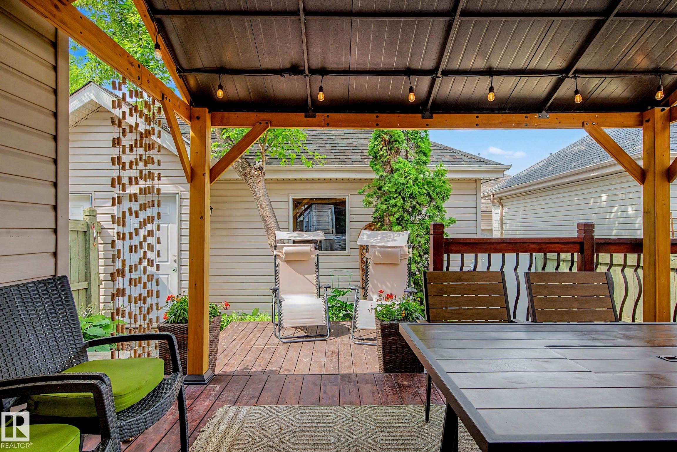 Covered wood-finish deck featuring a durable metal roof, exposed wood beams, and integrated string lighting - 9130 100A Avenue Nw, Edmonton, AB - Outdoor With Deck Patio Veranda With Exterior