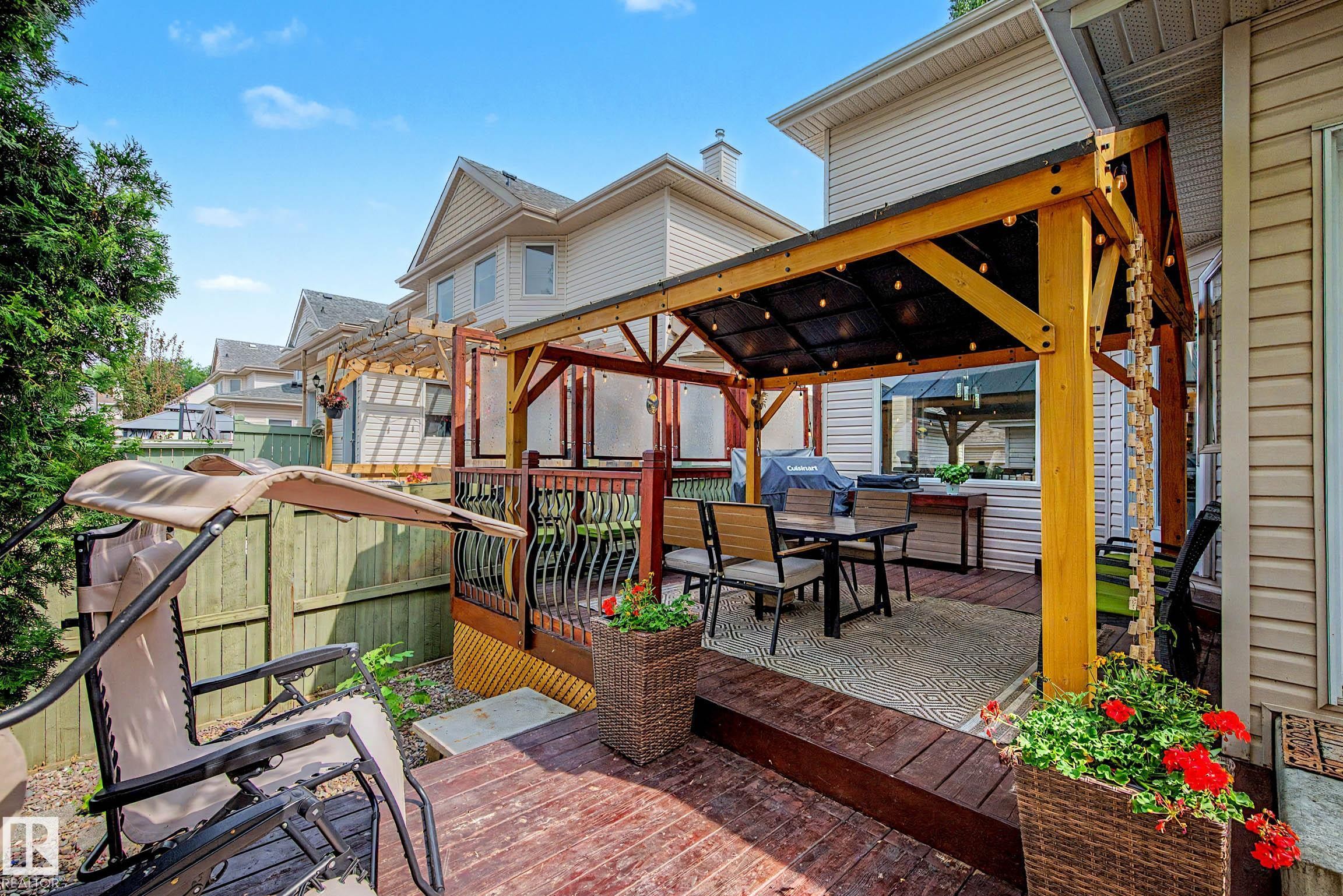 Multi-level wooden deck featuring a covered outdoor dining area with string lighting, a built-in outdoor kitchen unit, and a pergola structure - 9130 100A Avenue Nw, Edmonton, AB - Outdoor With Deck Patio Veranda With Exterior