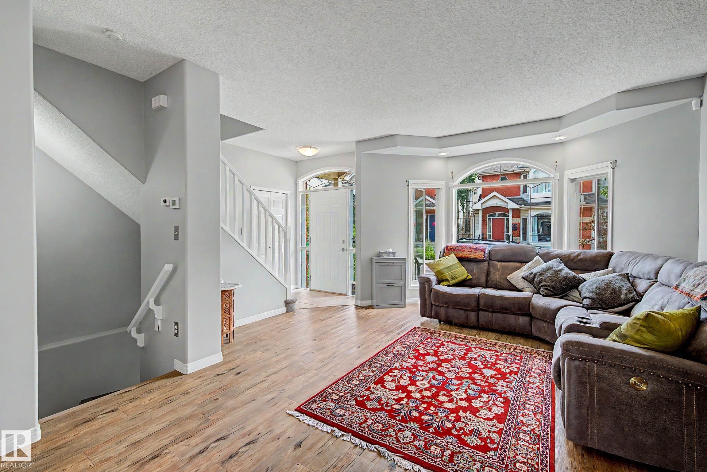 Spacious living area featuring wood-finish flooring, a prominent bay window, and a staircase with white railing - 9130 100A Avenue Nw, Edmonton, AB - Indoor Photo Showing Living Room