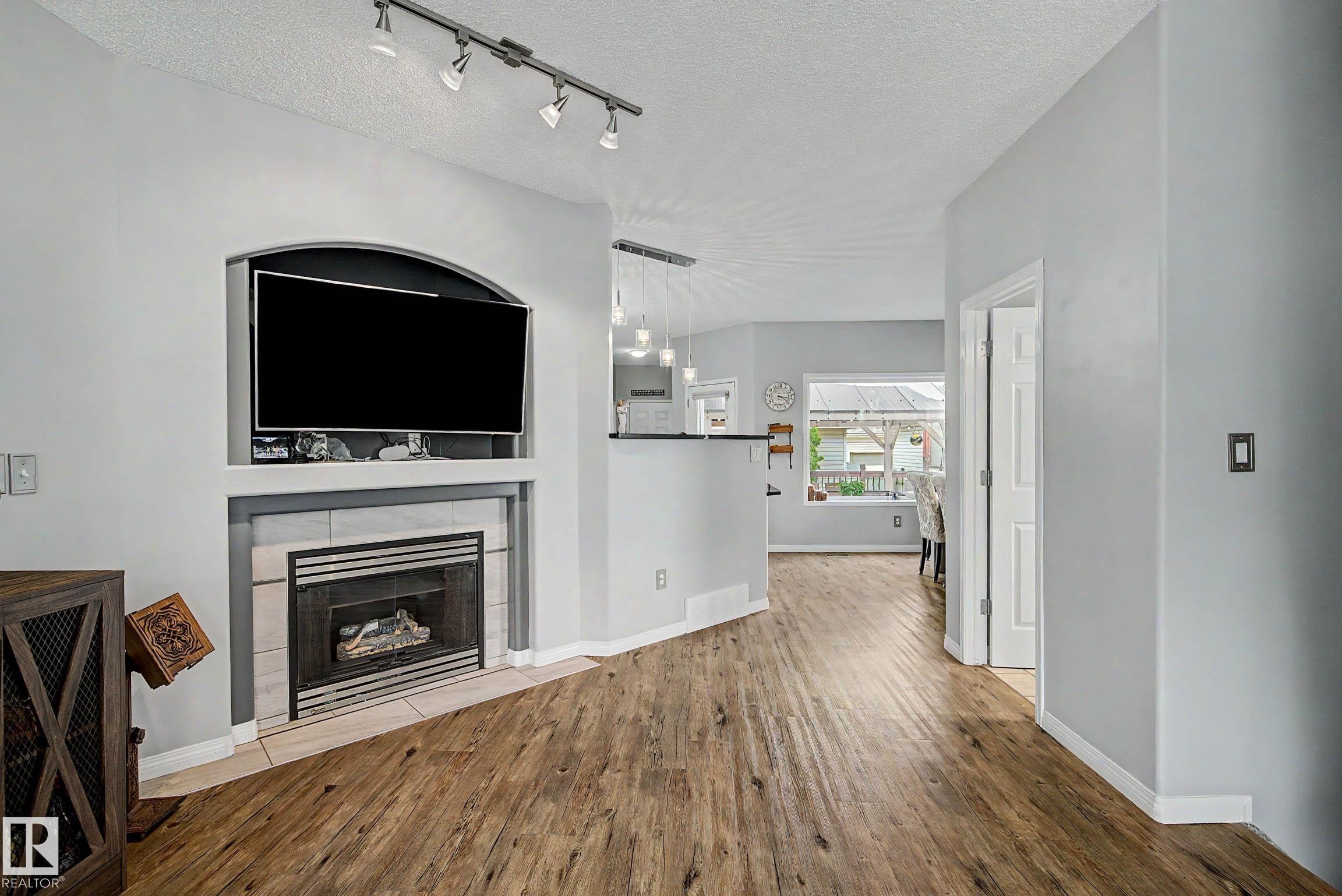 Living area featuring wood-finish flooring, a fireplace with tile surround, and an integrated media niche - 9130 100A Avenue Nw, Edmonton, AB - Indoor With Fireplace
