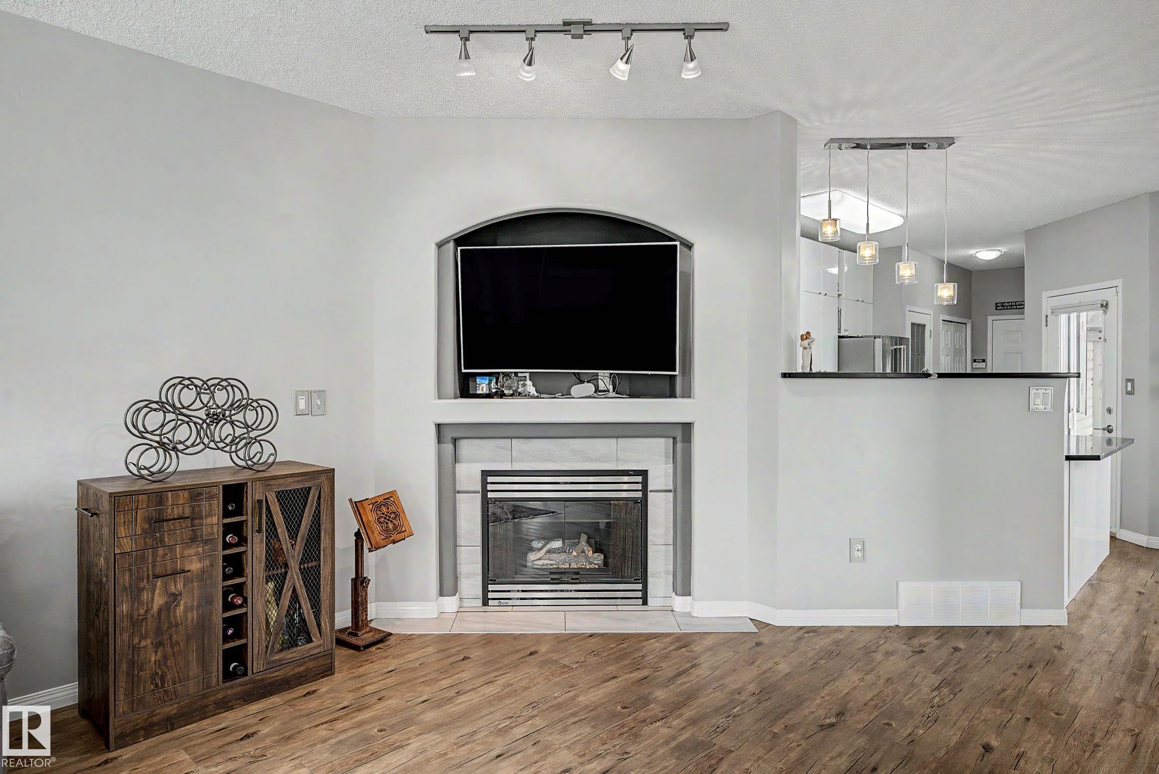 Living area featuring a fireplace with a tiled surround and mantel, wood-finish flooring, and recessed ceiling lighting - 9130 100A Avenue Nw, Edmonton, AB - Indoor Photo Showing Living Room With Fireplace