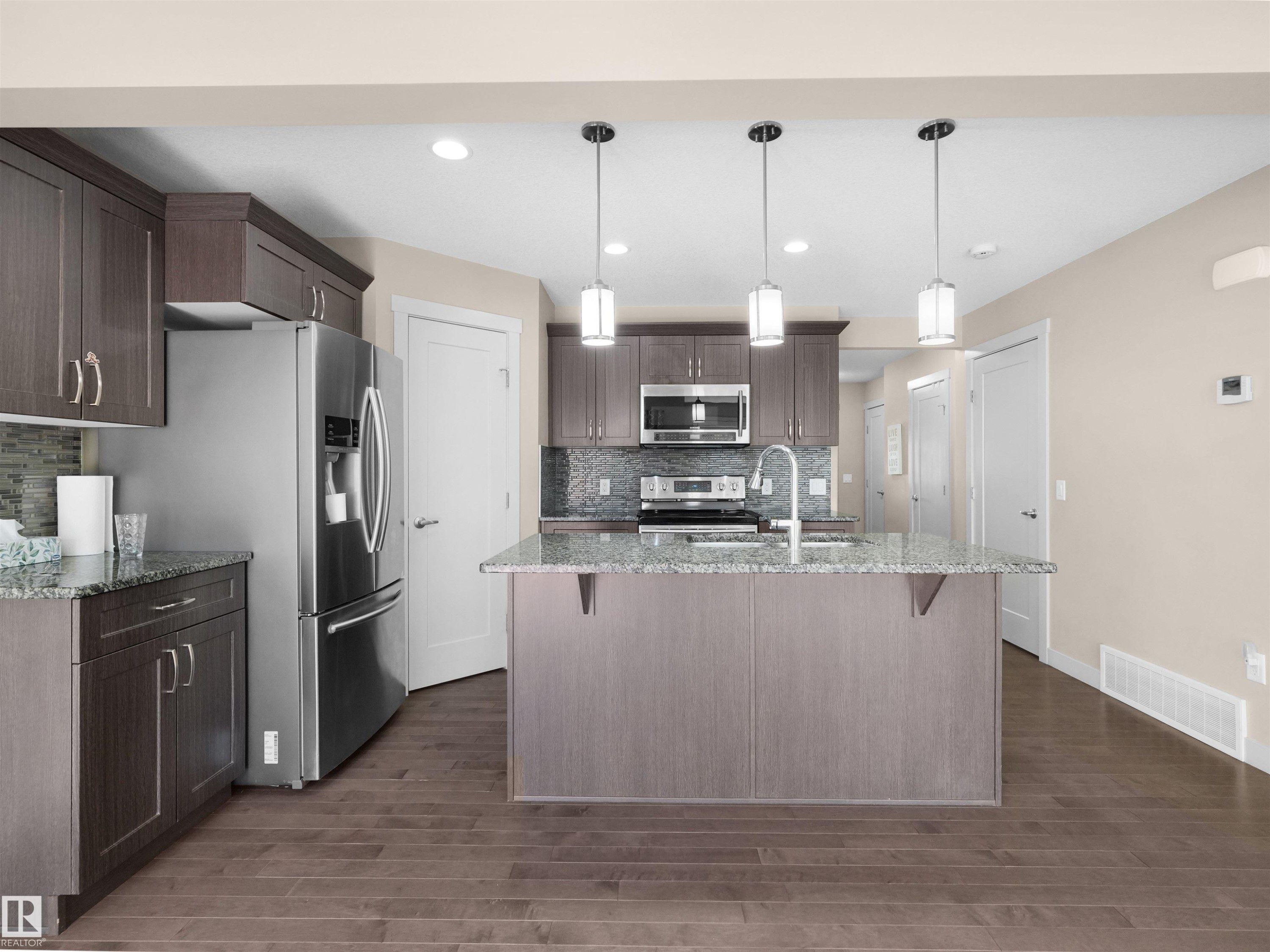 Kitchen featuring wood-finish flooring, dark wood cabinetry, and light-toned countertops - 4487 Annett Common Sw, Edmonton, AB - Indoor Photo Showing Kitchen With Stainless Steel Kitchen With Upgraded Kitchen