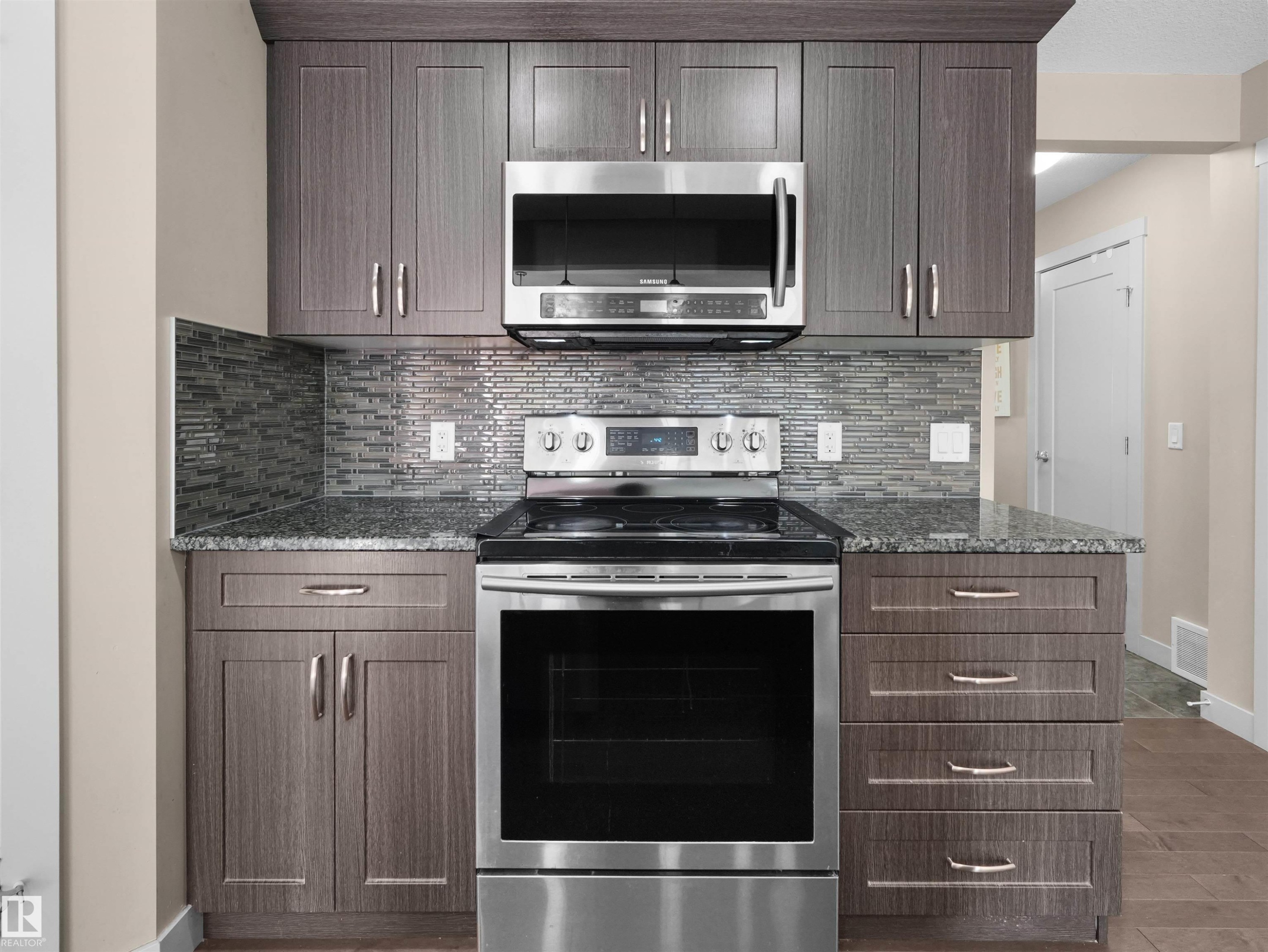 Contemporary kitchen featuring stainless steel appliances, grey wood-finish cabinetry, a mosaic tile backsplash, and stone countertops - 4487 Annett Common Sw, Edmonton, AB - Indoor Photo Showing Kitchen With Upgraded Kitchen