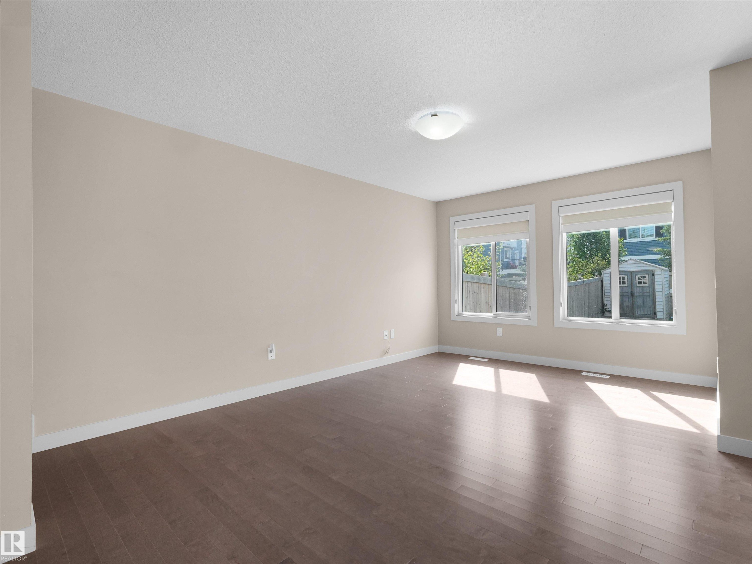 Spacious room featuring wood-finish flooring, neutral-toned walls, and white baseboards - 4487 Annett Common Sw, Edmonton, AB - Indoor Photo Showing Other Room
