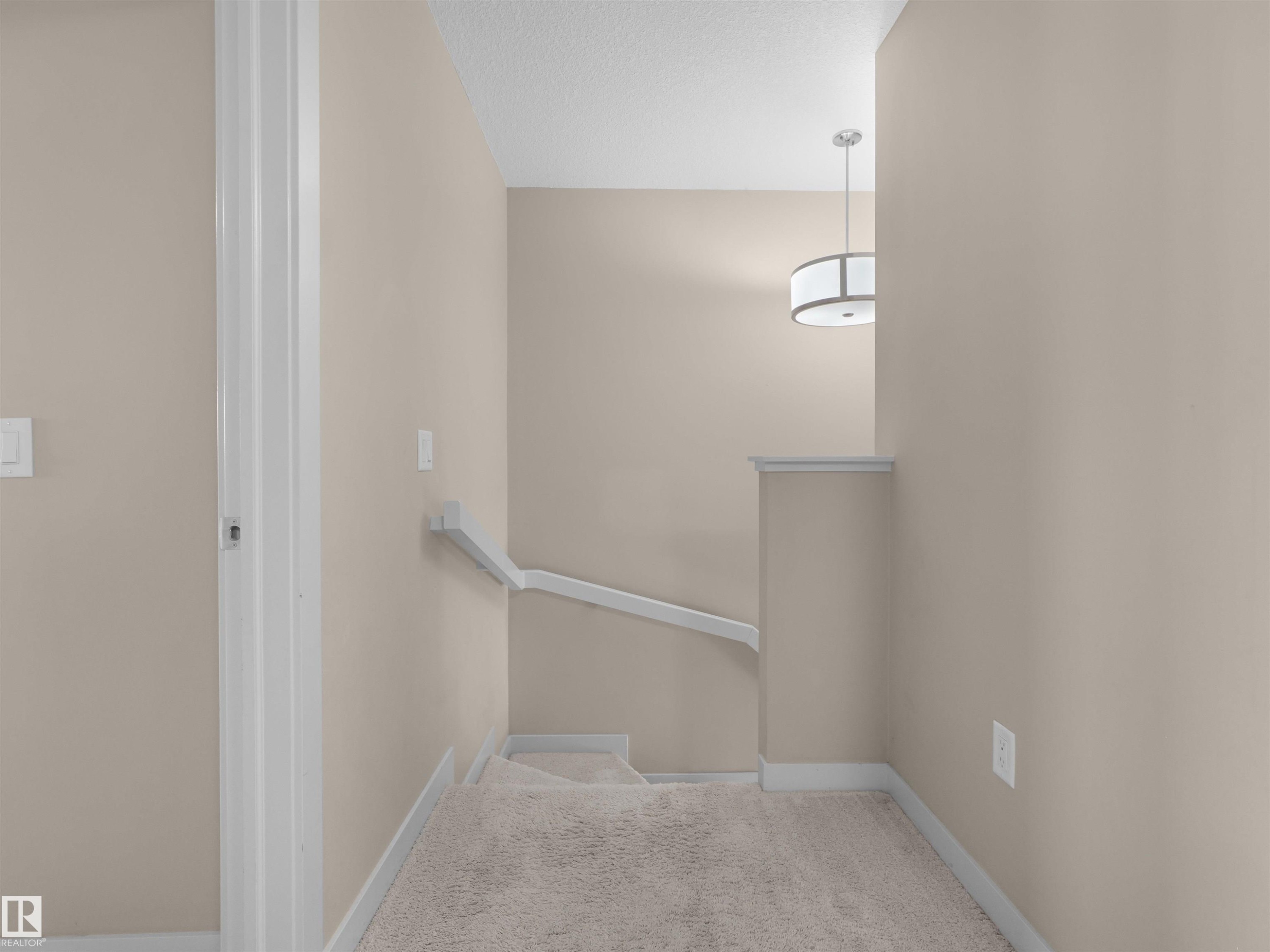 Carpeted staircase featuring a white handrail, neutral wall paint, and a contemporary ceiling pendant light - 4487 Annett Common Sw, Edmonton, AB - Indoor Photo Showing Other Room
