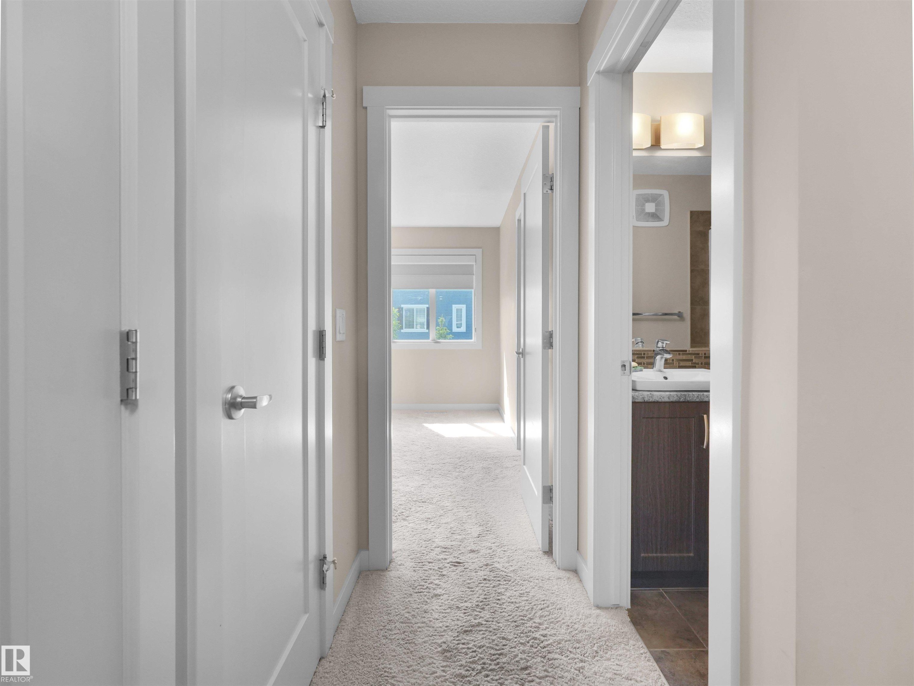 Hallway with light beige walls and plush carpet flooring, featuring white paneled doors with brushed nickel hardware - 4487 Annett Common Sw, Edmonton, AB - Indoor Photo Showing Other Room