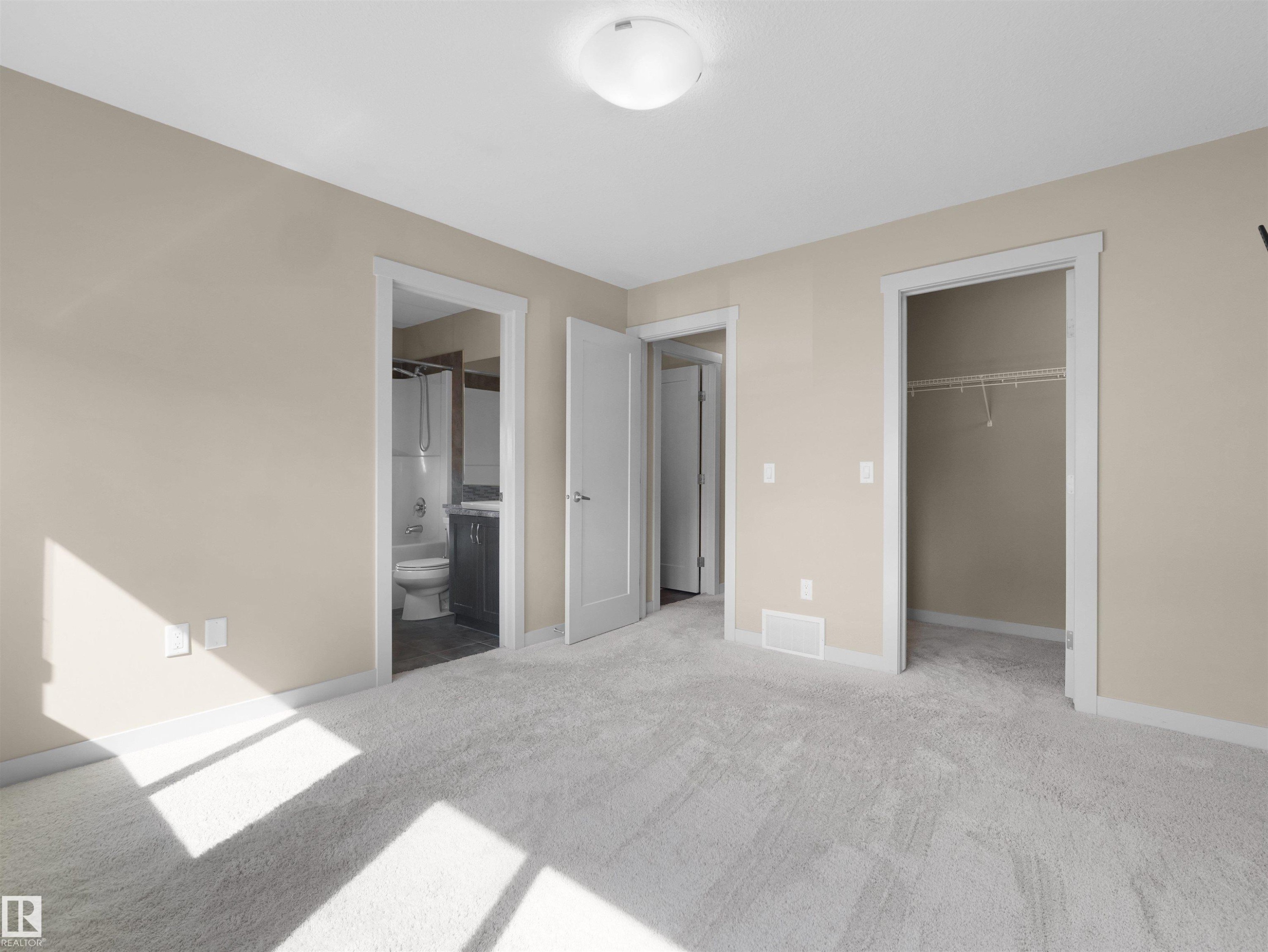 Carpeted room featuring a ceiling-mounted light fixture, neutral wall paint, white trim, and a white interior door - 4487 Annett Common Sw, Edmonton, AB - Indoor Photo Showing Other Room