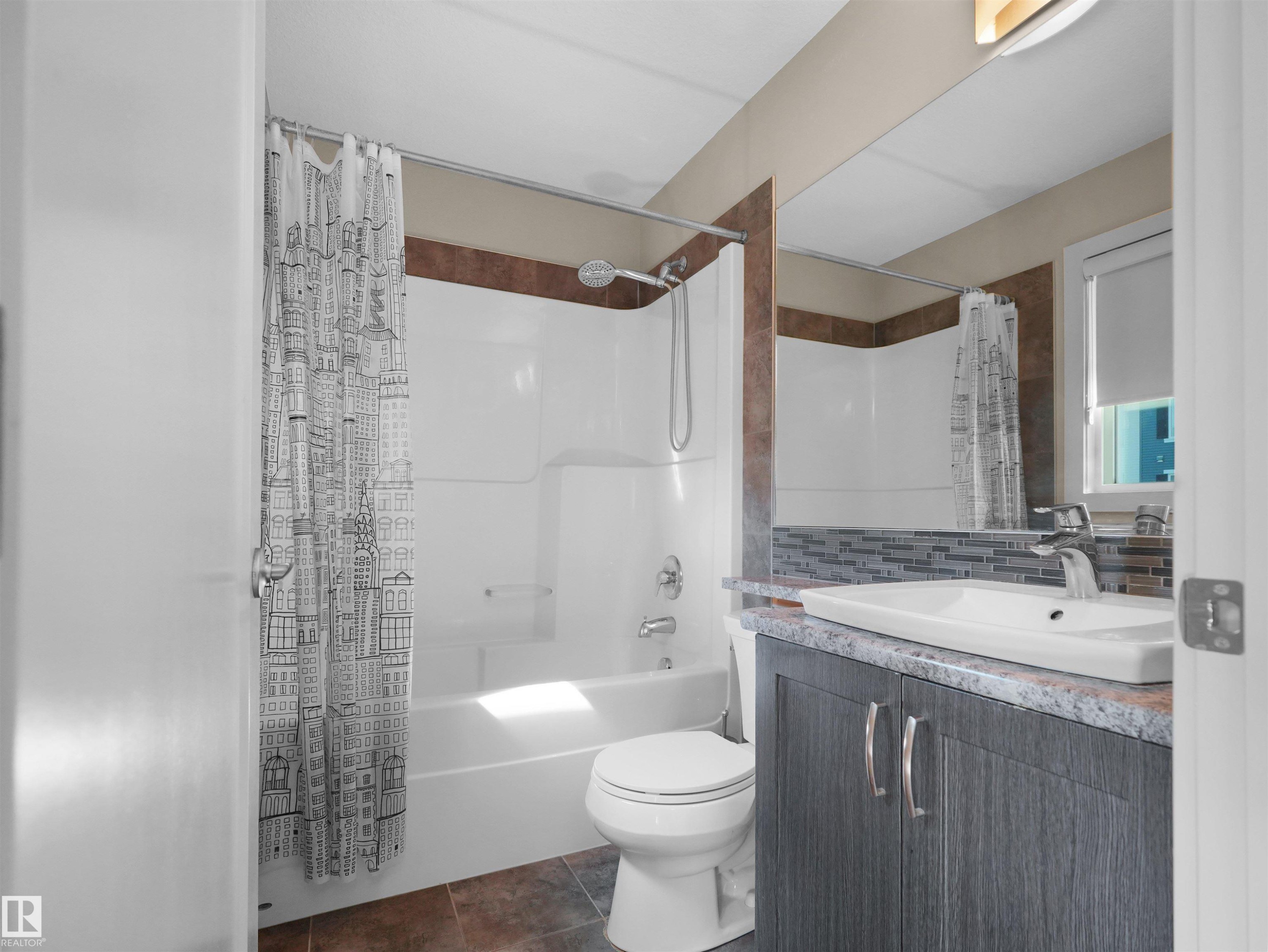 Bathroom featuring a white tub and shower combination, a vanity with a surface-mount sink, dark wood-finish cabinetry, a large wall mirror, and modern mosaic tile backsplash - 4487 Annett Common Sw, Edmonton, AB - Indoor Photo Showing Bathroom