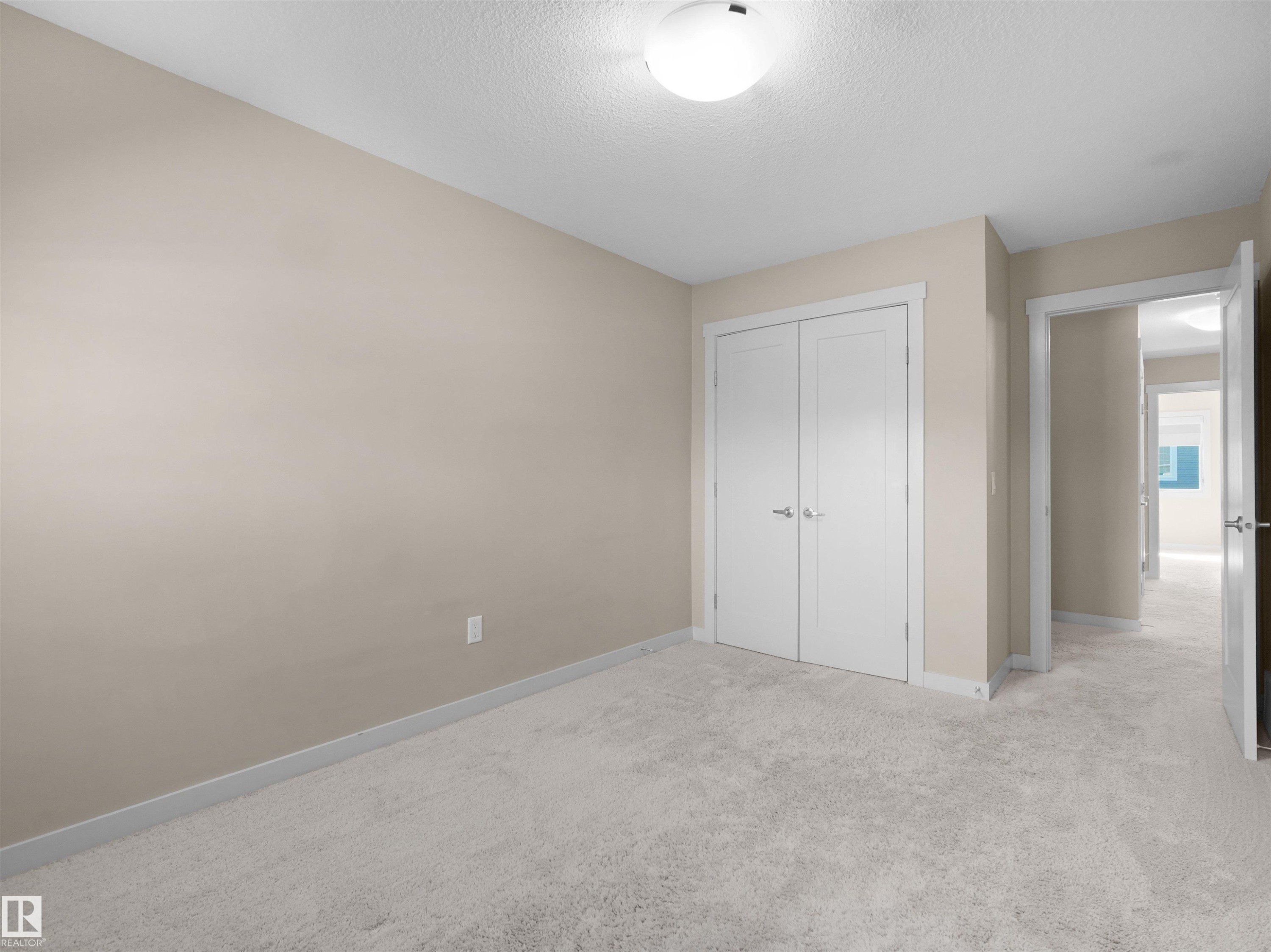 Neutral-toned room featuring light-colored carpeting, a double-door closet with white trim, and a flush-mount ceiling light fixture - 4487 Annett Common Sw, Edmonton, AB - Indoor Photo Showing Other Room