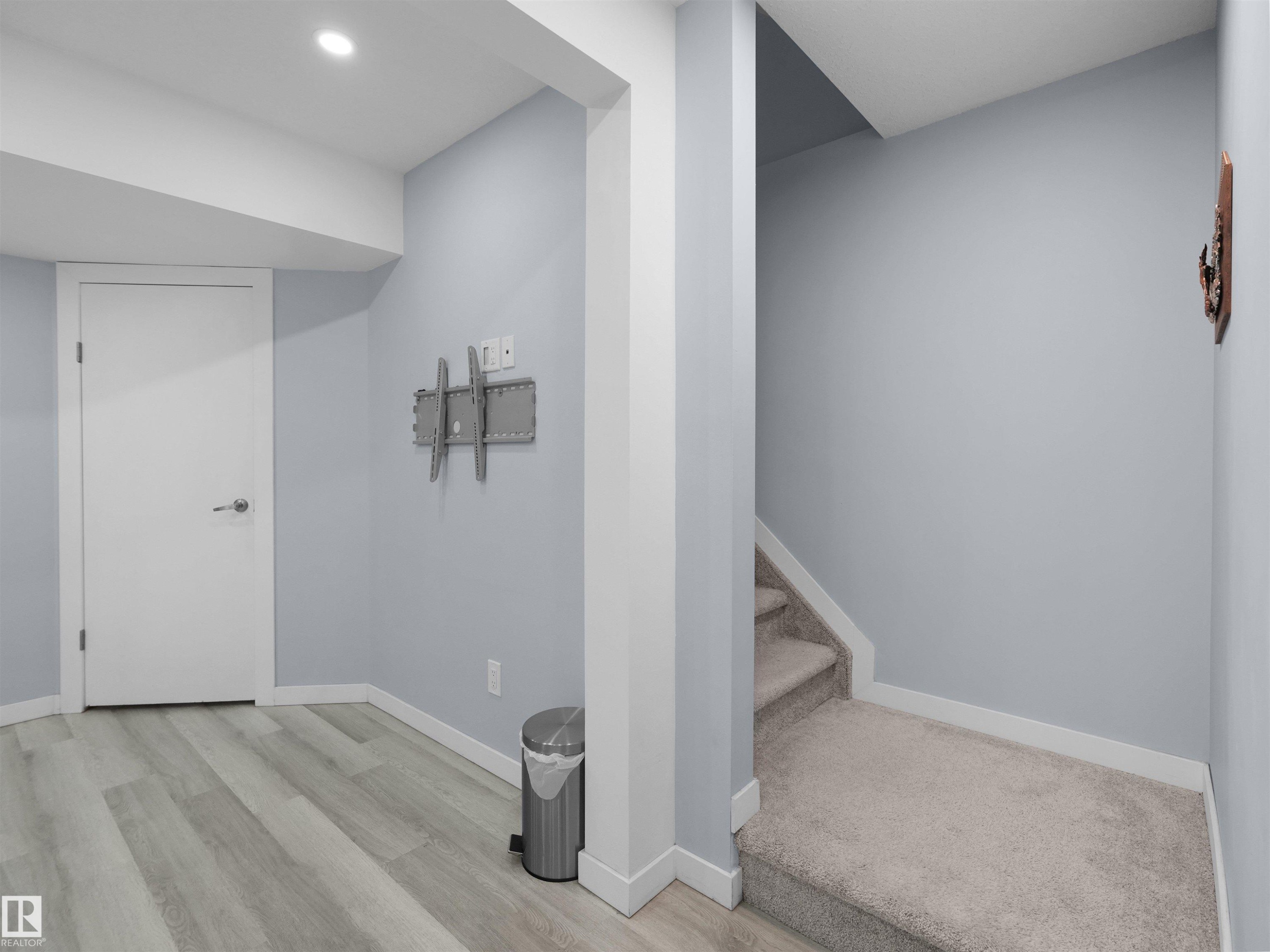 Basement area featuring wood-finish flooring, light blue painted walls, and white trim - 4487 Annett Common Sw, Edmonton, AB - Indoor Photo Showing Other Room
