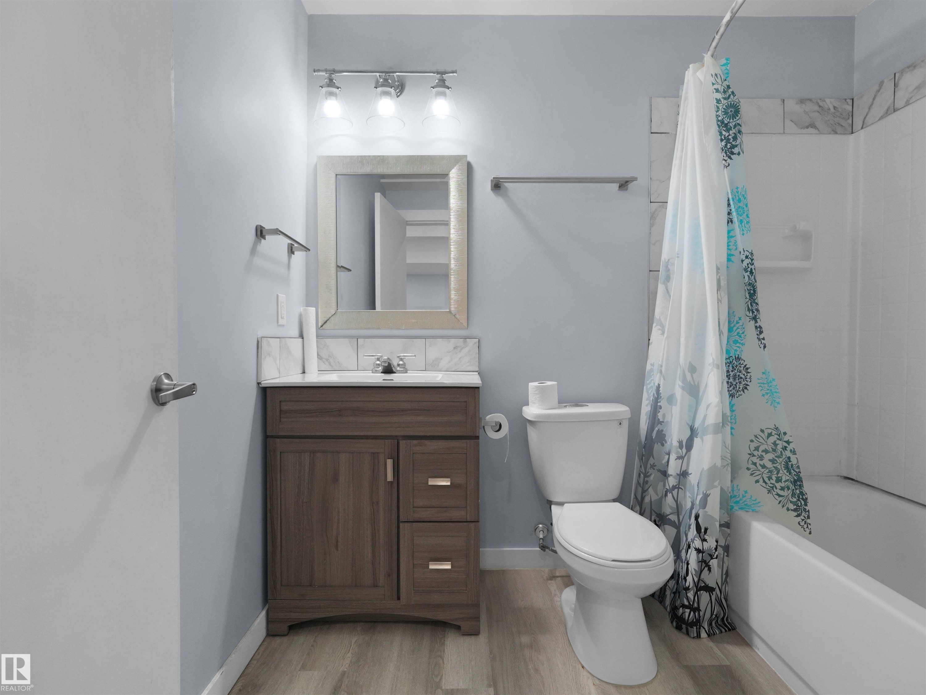 Bathroom featuring a wood-finish vanity with a white countertop and integrated sink, framed mirror, and chrome fixtures - 4487 Annett Common Sw, Edmonton, AB - Indoor Photo Showing Bathroom