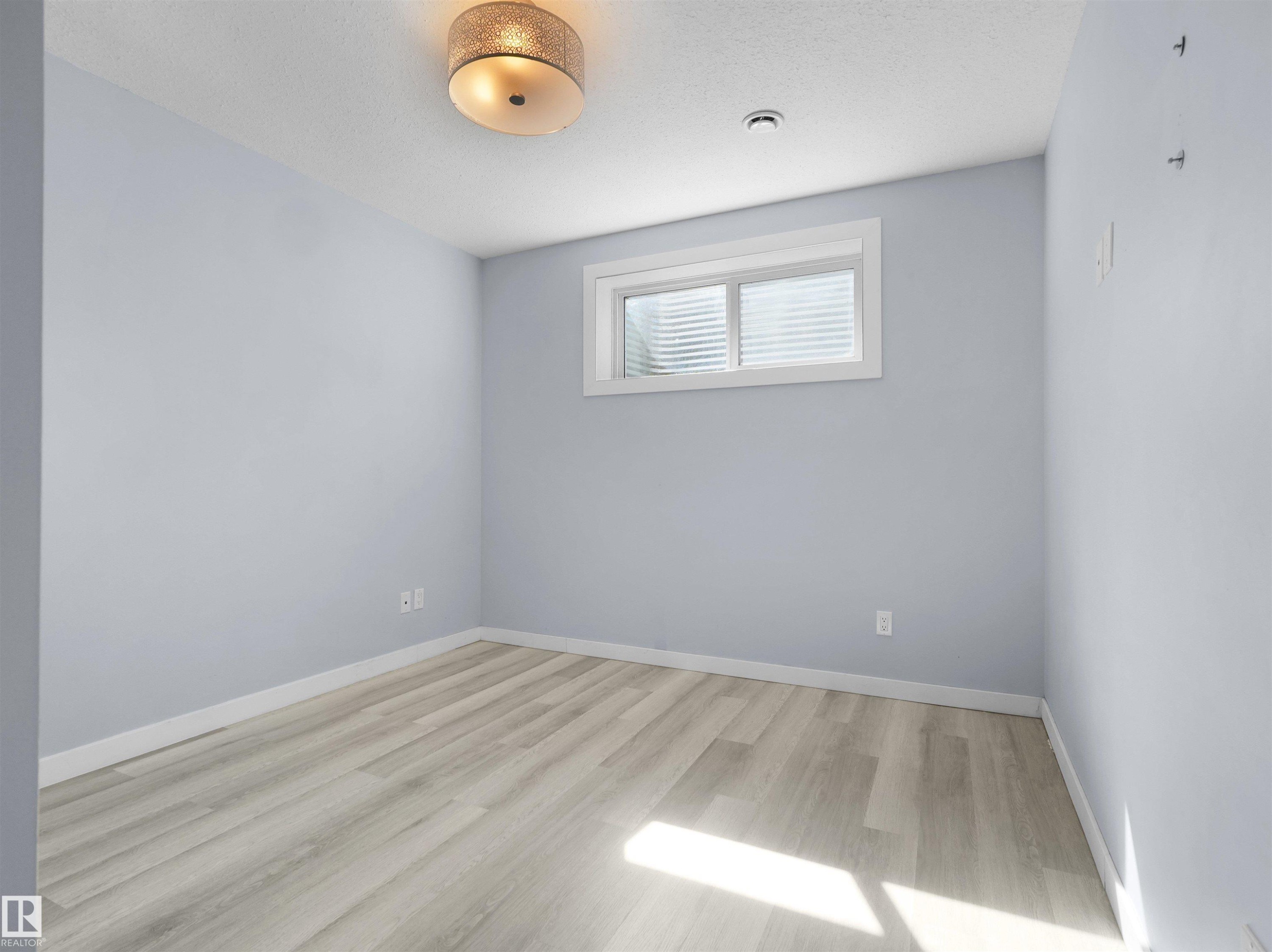 Spacious room featuring light wood-finish flooring, light blue painted walls, a flush-mount ceiling light fixture, and a window with horizontal blinds - 4487 Annett Common Sw, Edmonton, AB - Indoor Photo Showing Other Room