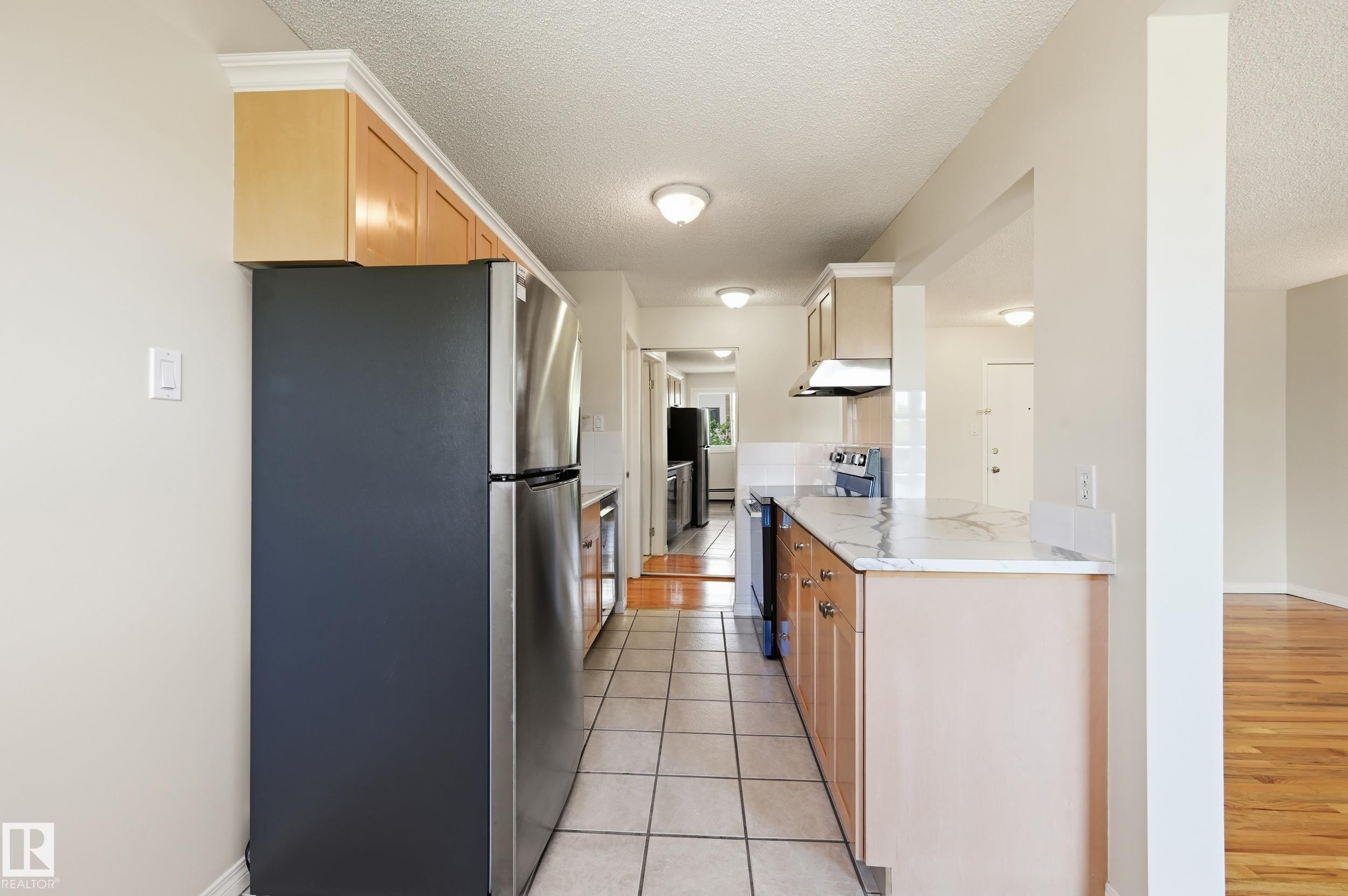 Galley kitchen featuring natural wood cabinetry, stainless steel appliances, and a marble-look countertop - #433 11217 103 Av Nw, Edmonton, AB - Indoor Photo Showing Kitchen