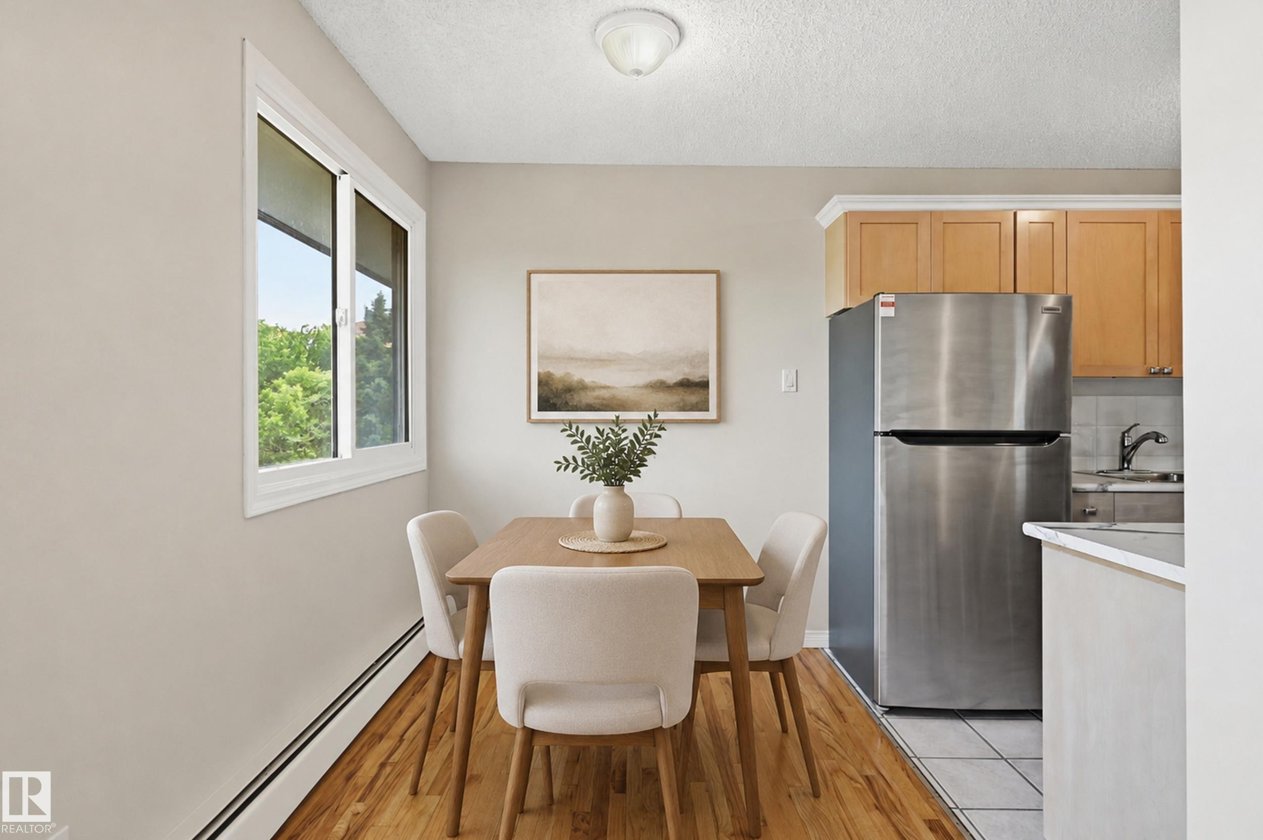 Dining area featuring wood-finish flooring, a large window, a ceiling-mounted light fixture, and neutral wall tones - #433 11217 103 Av Nw, Edmonton, AB - Indoor