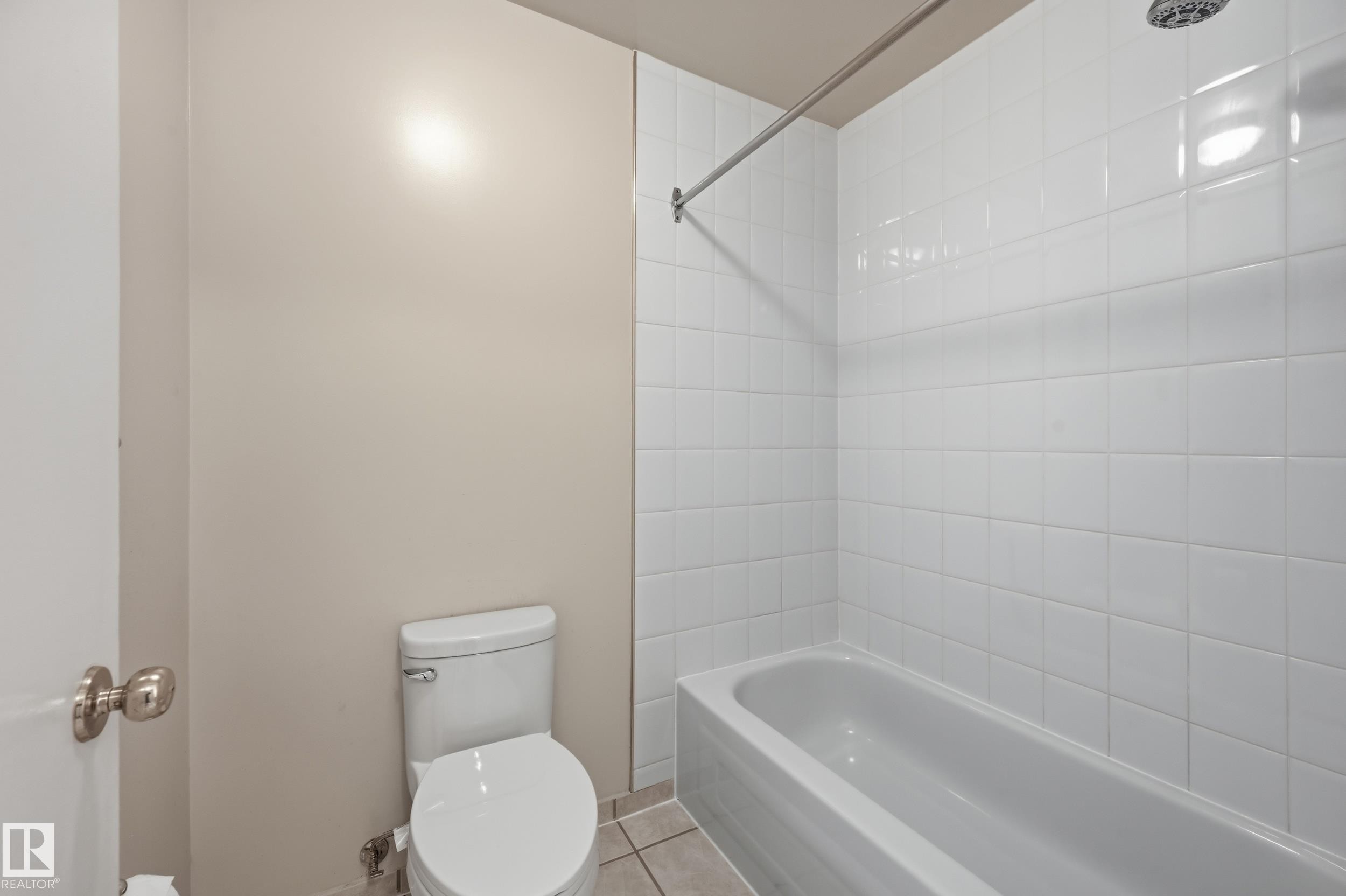 Bathroom featuring a full-size bathtub, white subway tile surround, white toilet, and tile flooring - #433 11217 103 Av Nw, Edmonton, AB - Indoor Photo Showing Bathroom