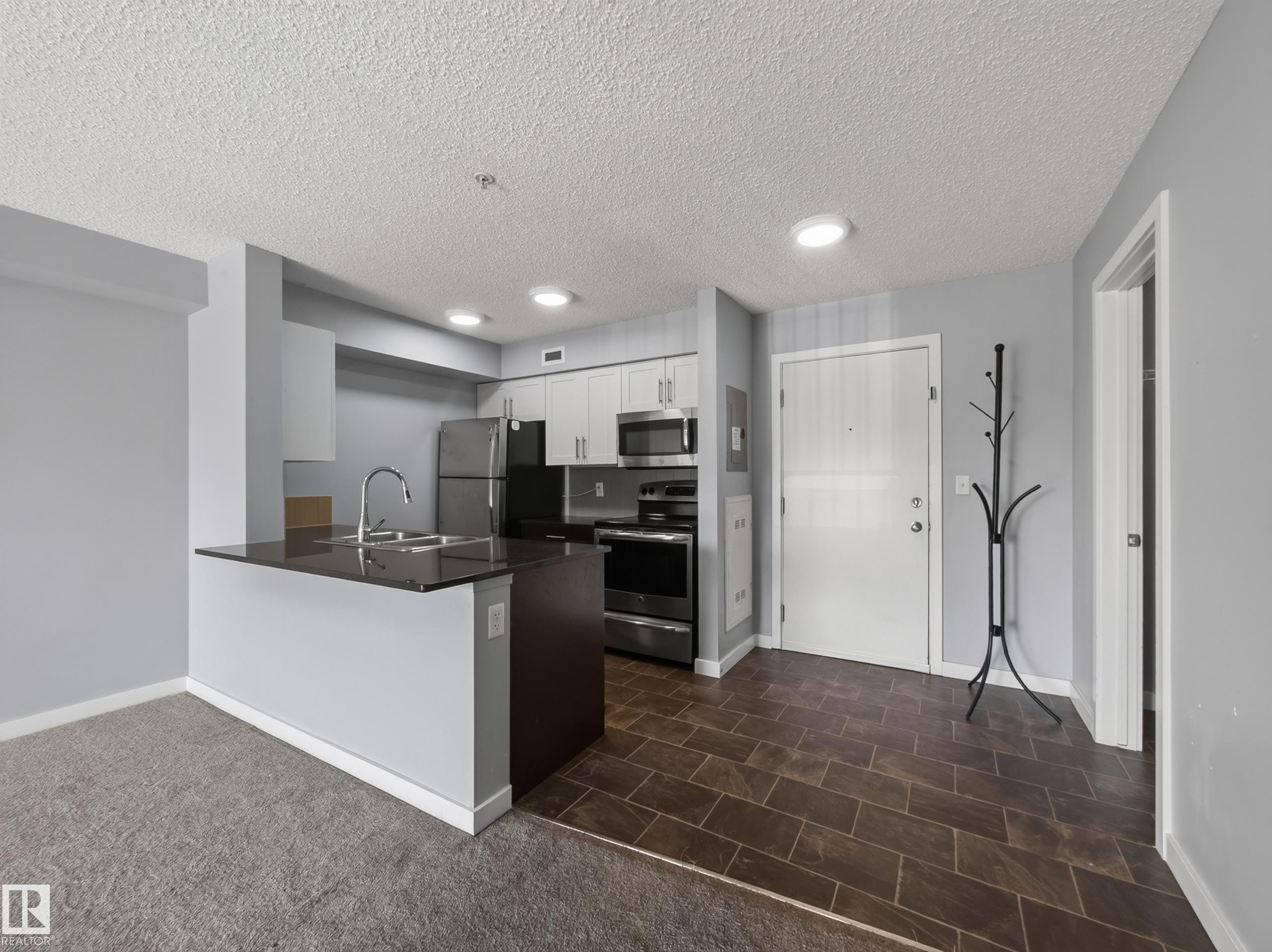 Kitchen featuring stainless steel appliances, dark countertop, and light cabinetry - #217 12045 22 Av Sw, Edmonton, AB - Indoor Photo Showing Kitchen With Stainless Steel Kitchen