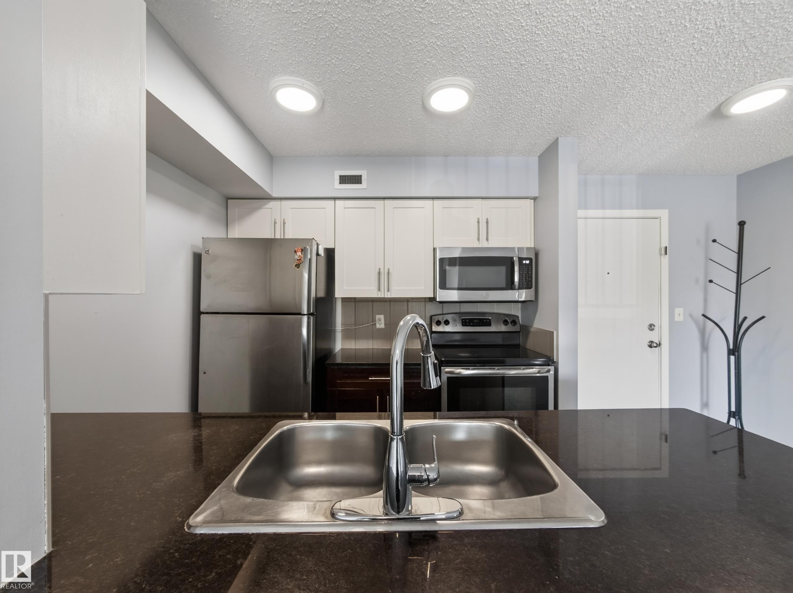Kitchen featuring stainless steel appliances, light cabinetry, and dark countertops - #217 12045 22 Av Sw, Edmonton, AB - Indoor Photo Showing Kitchen With Stainless Steel Kitchen With Double Sink