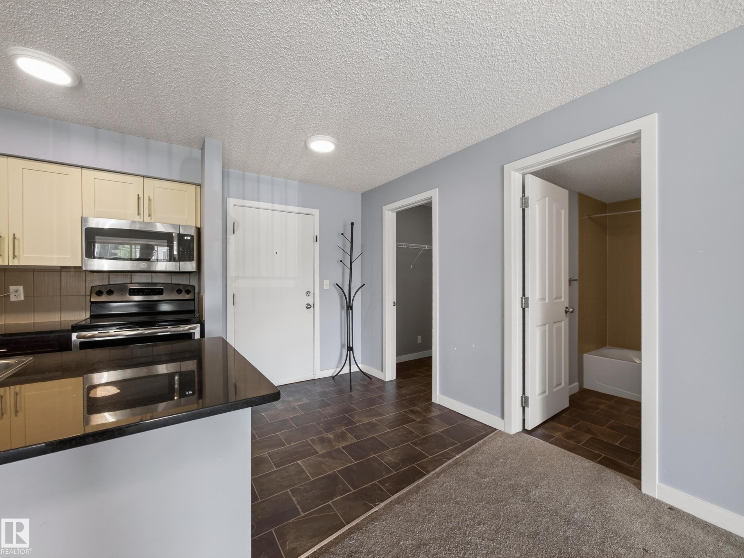 Contemporary kitchen featuring stainless steel appliances, light-toned cabinetry, and dark countertops - #217 12045 22 Av Sw, Edmonton, AB - Indoor Photo Showing Kitchen