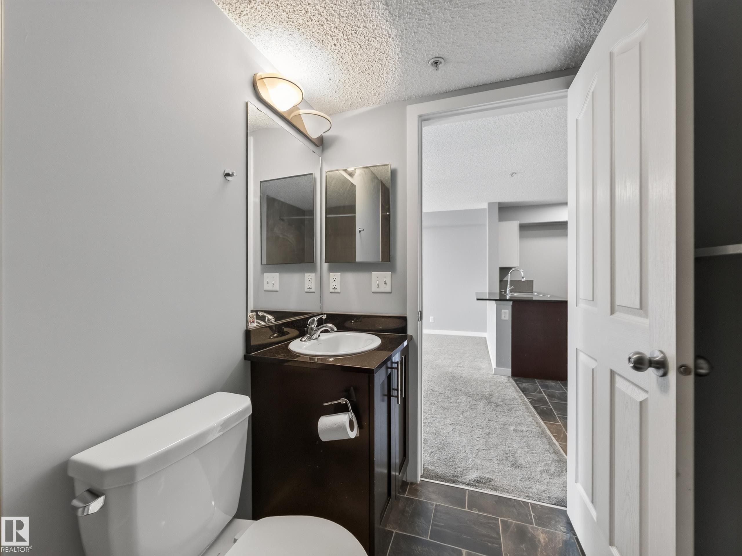 Bathroom featuring a dark wood-finish vanity, white ceramic sink, and a wall-mounted light fixture - #217 12045 22 Av Sw, Edmonton, AB - Indoor Photo Showing Bathroom