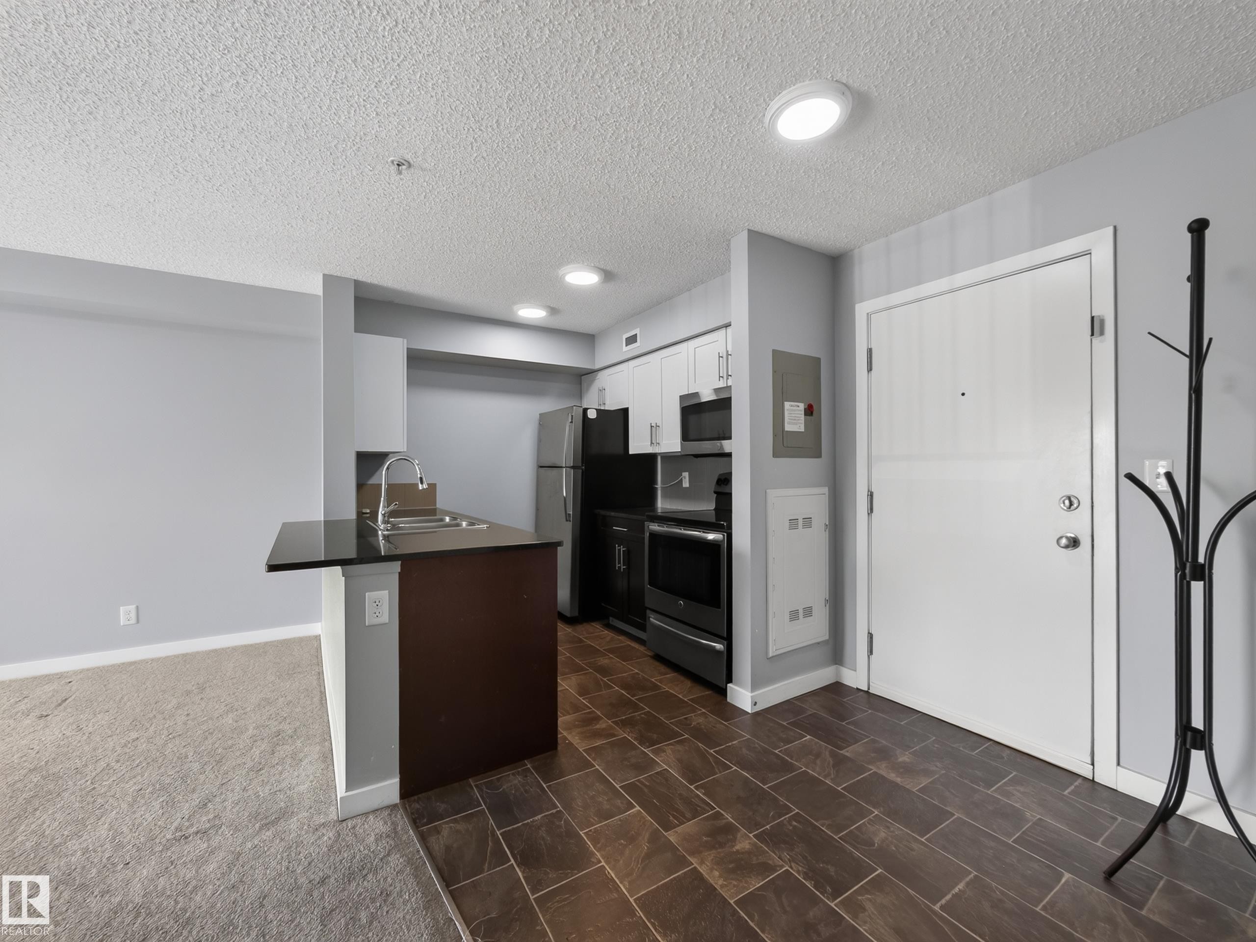 Kitchenette featuring white cabinetry, black appliances, a stainless steel sink, and a black countertop on a breakfast bar - #217 12045 22 Av Sw, Edmonton, AB - Indoor Photo Showing Kitchen