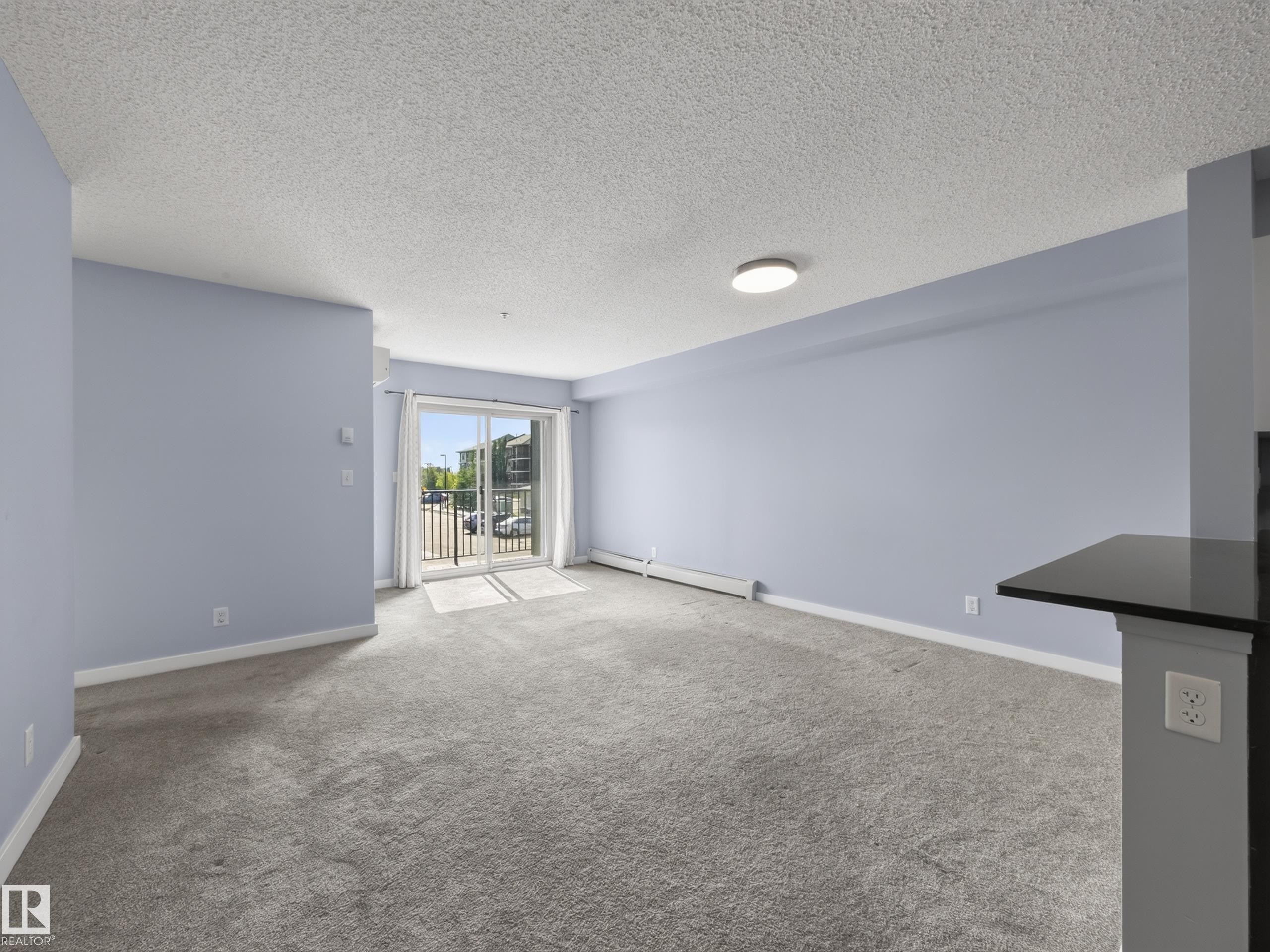 Spacious room featuring light blue walls, grey carpeting, and a sliding glass door leading to a balcony - #217 12045 22 Av Sw, Edmonton, AB - Indoor Photo Showing Other Room