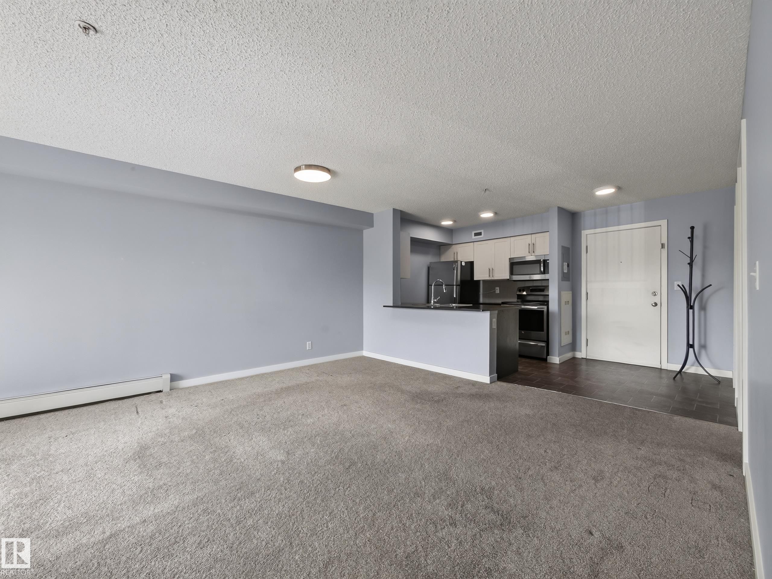 Open-concept living space with light gray carpeting and blue-gray walls - #217 12045 22 Av Sw, Edmonton, AB - Indoor