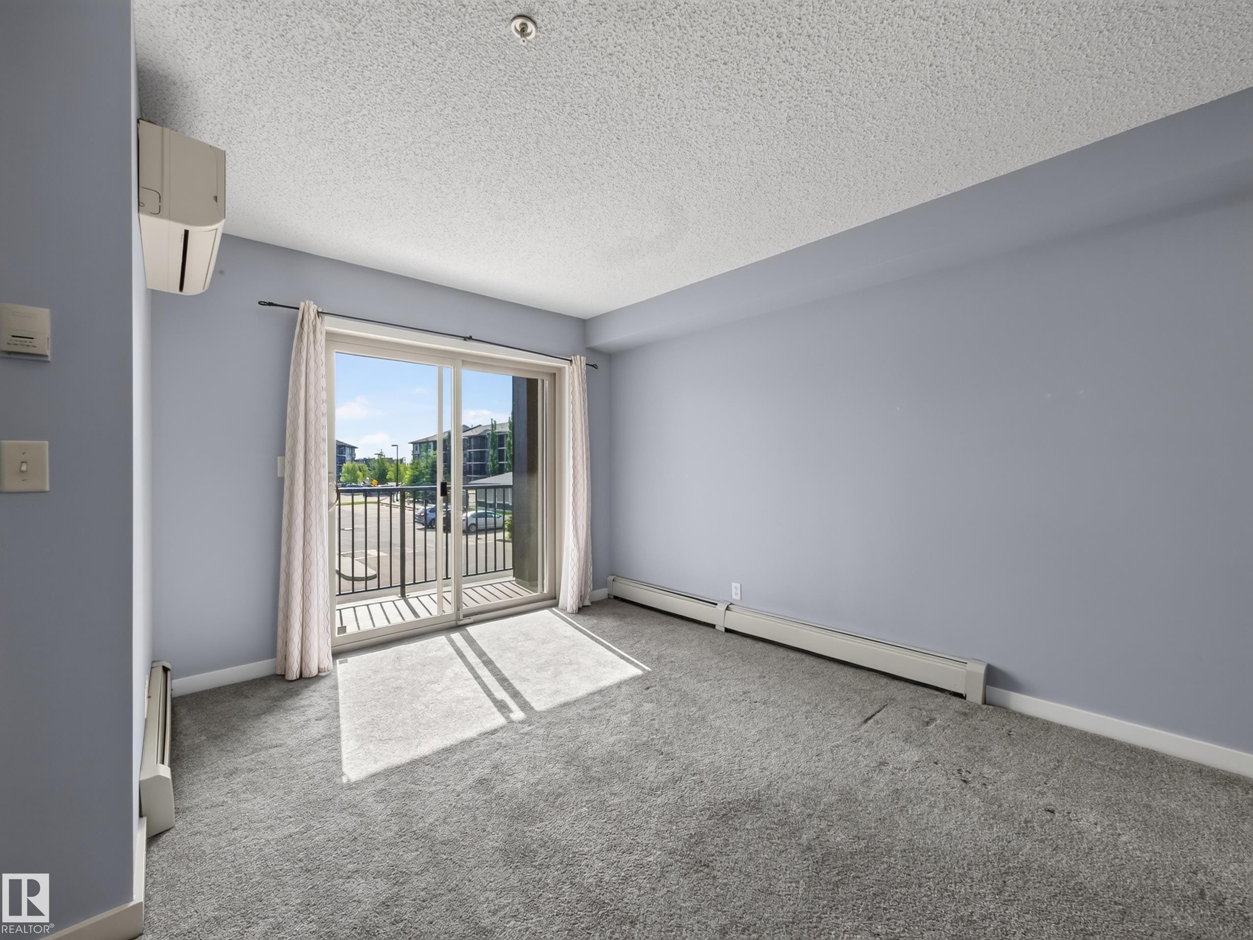 Sliding glass doors opening to an outdoor balcony with black metal railings - #217 12045 22 Av Sw, Edmonton, AB - Indoor Photo Showing Other Room