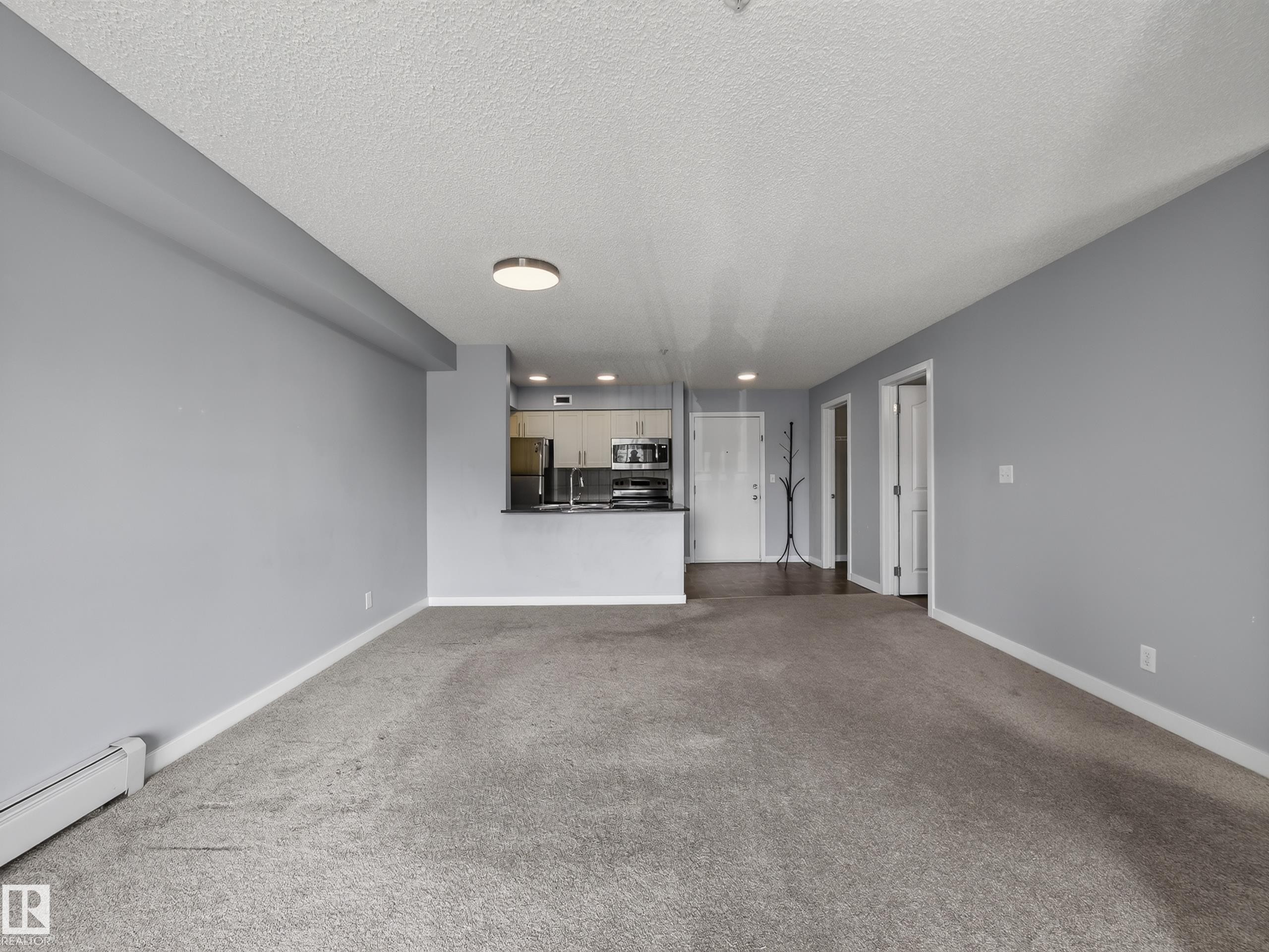 Open-concept living space featuring light gray walls, textured carpet flooring, and white trim - #217 12045 22 Av Sw, Edmonton, AB - Indoor Photo Showing Other Room
