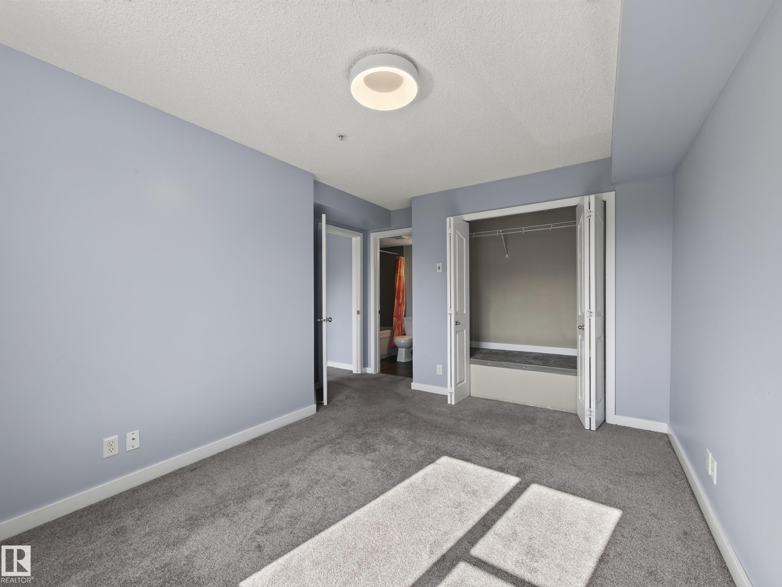 Carpeted room featuring light blue walls, a ceiling-mounted light fixture, white trim, and a bi-fold closet with shelving - #217 12045 22 Av Sw, Edmonton, AB - Indoor Photo Showing Other Room