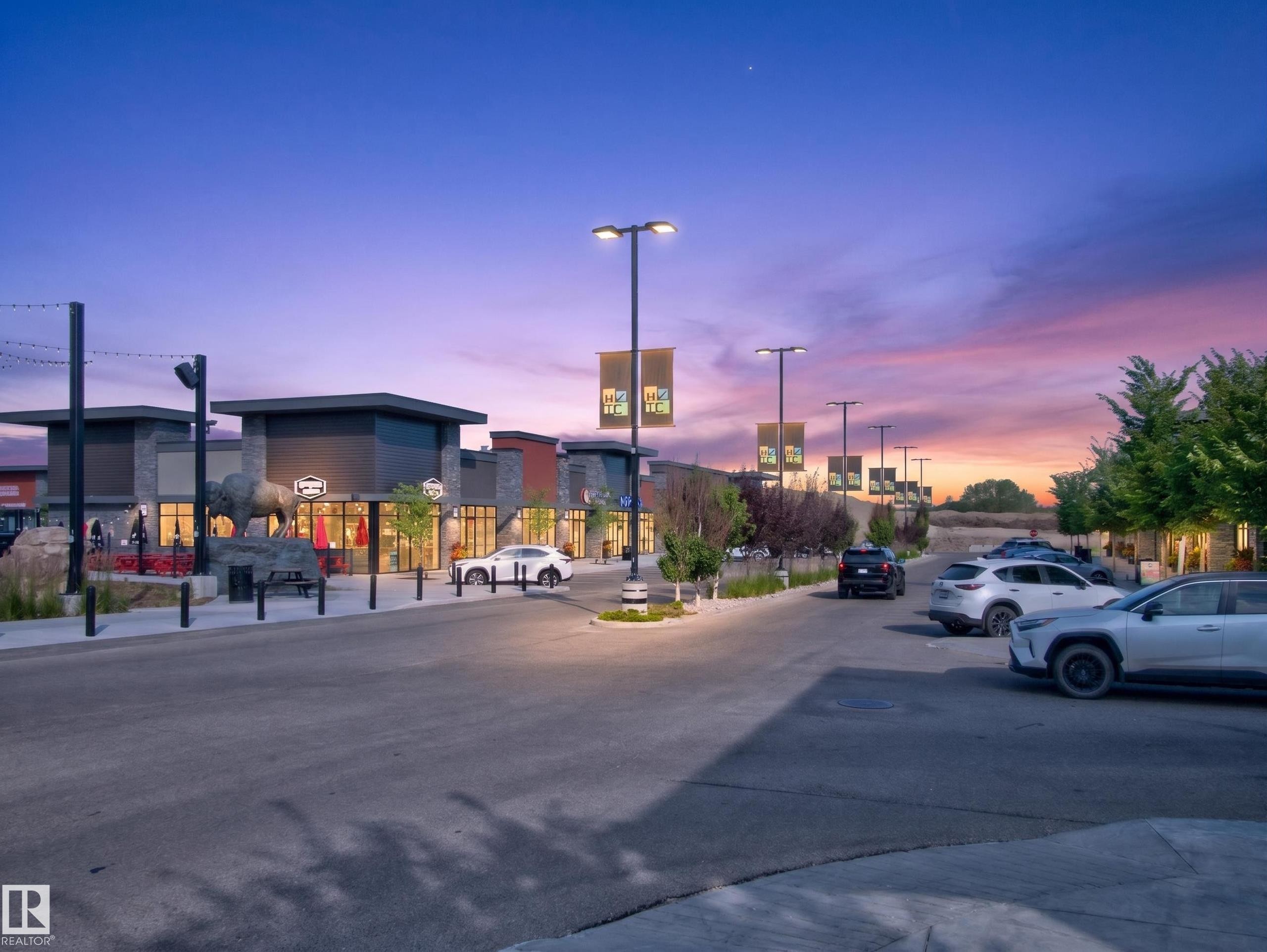 Retail frontage featuring modern architectural design with stone accents, storefront windows, and exterior lighting - #217 12045 22 Av Sw, Edmonton, AB - Outdoor