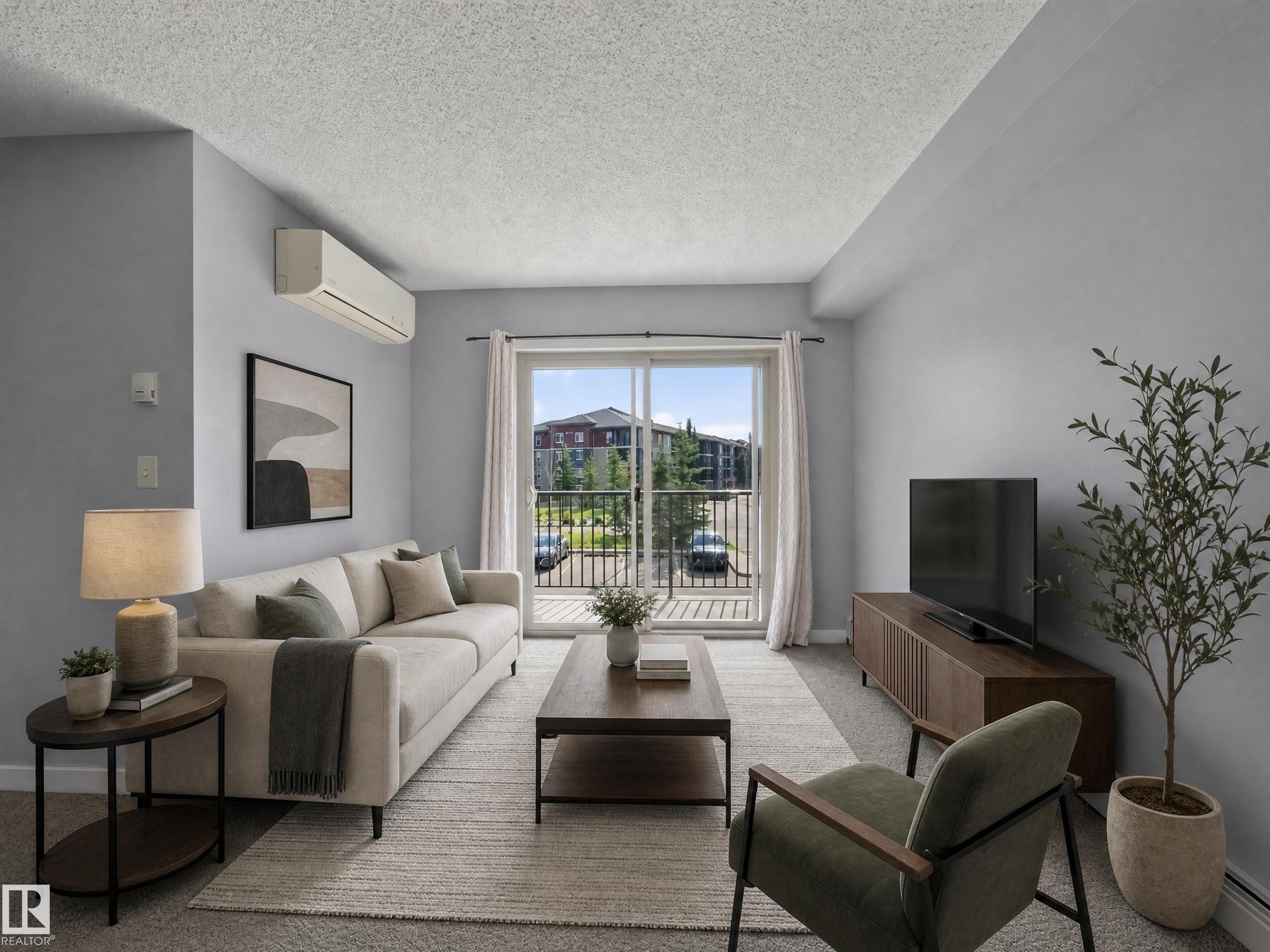 Living space featuring light gray walls, a split-system air conditioning unit, and a sliding glass door leading to a balcony with black metal railings - #217 12045 22 Av Sw, Edmonton, AB - Indoor Photo Showing Living Room