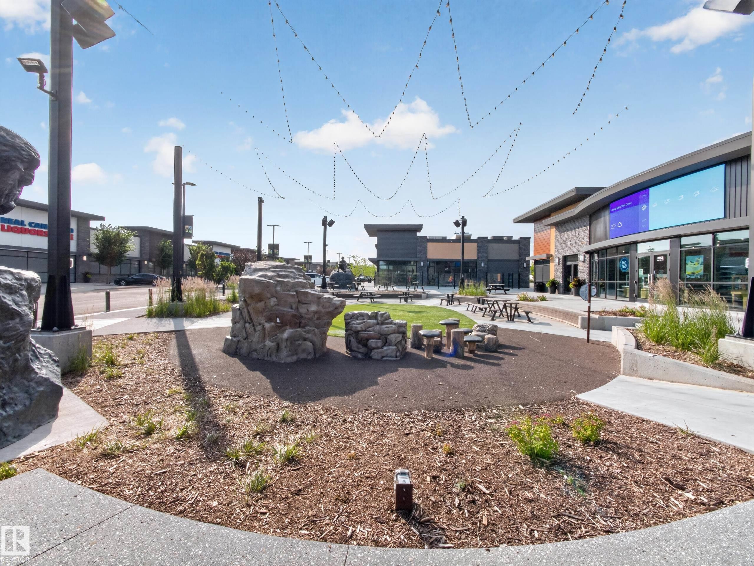 Modern mixed-use development featuring contemporary architecture, stone and wood-paneled facades, and a central green space - #217 12045 22 Av Sw, Edmonton, AB - Outdoor