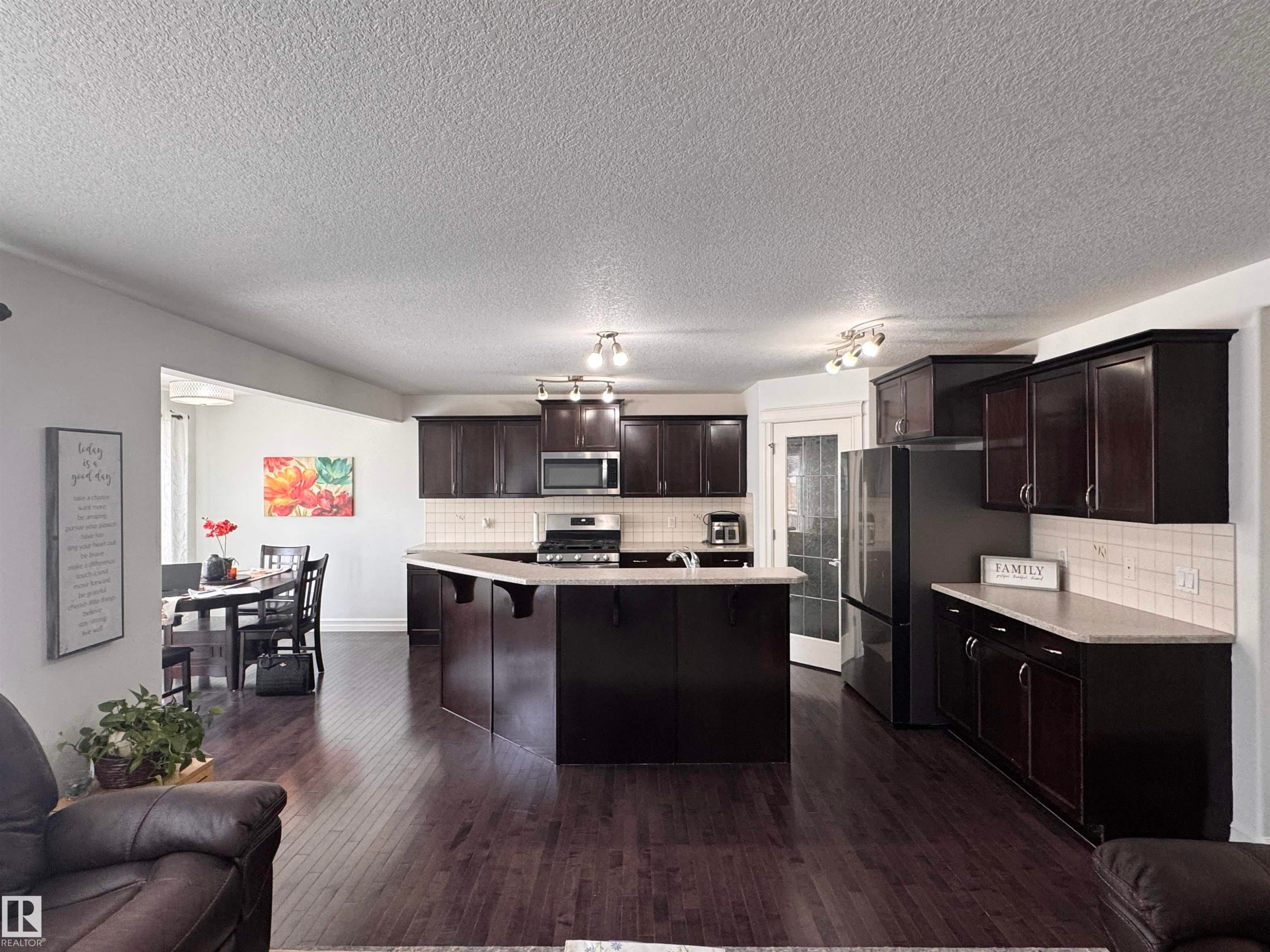 Kitchen featuring dark wood cabinetry, stainless steel appliances, a center island with seating, and light countertops - 1115 61 Street Sw, Edmonton, AB