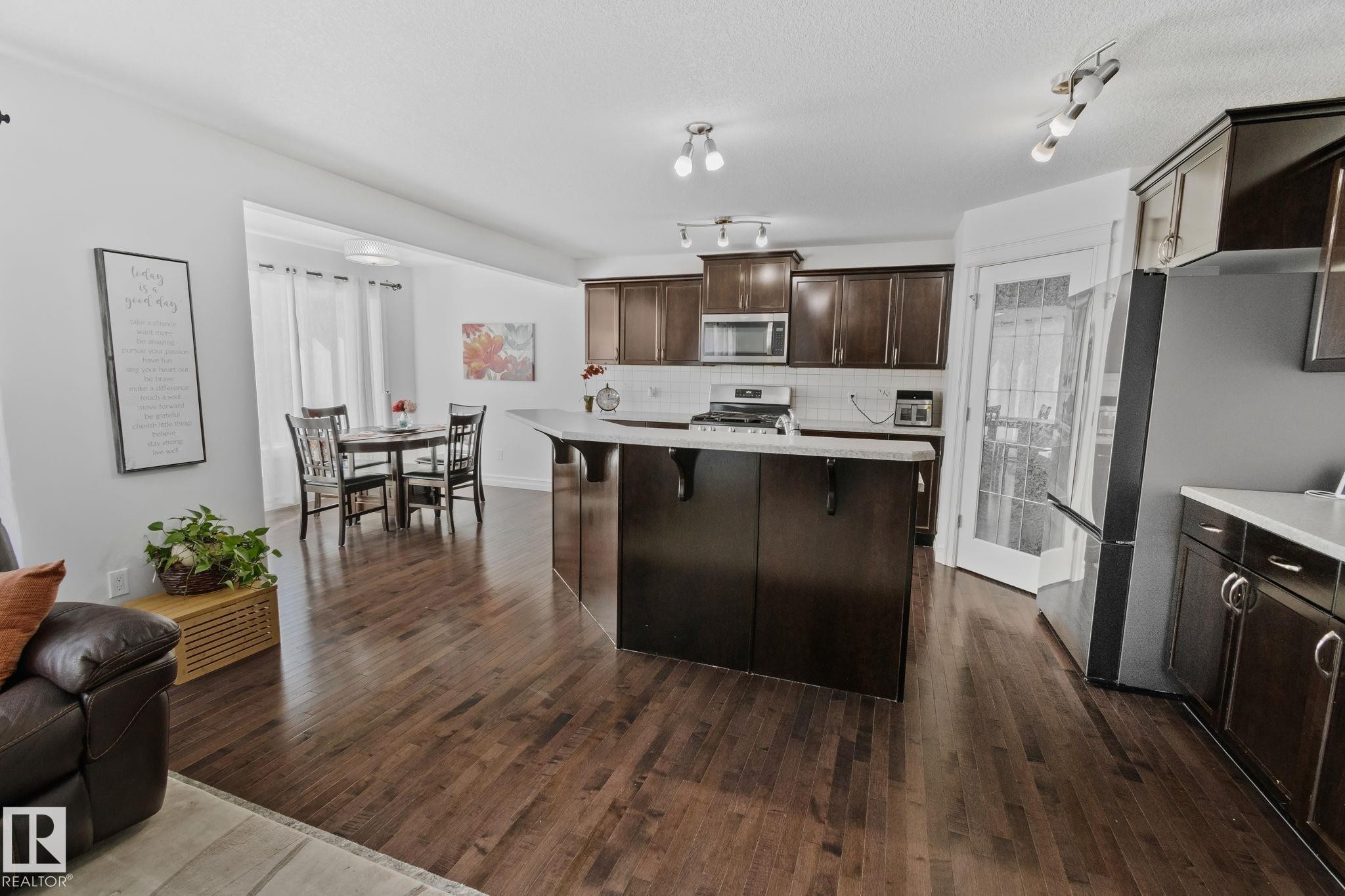 The property features rich hardwood flooring throughout, a kitchen with dark cabinetry, stainless steel appliances, and a central island with a light-colored countertop - 1115 61 Street Sw, Edmonton, AB