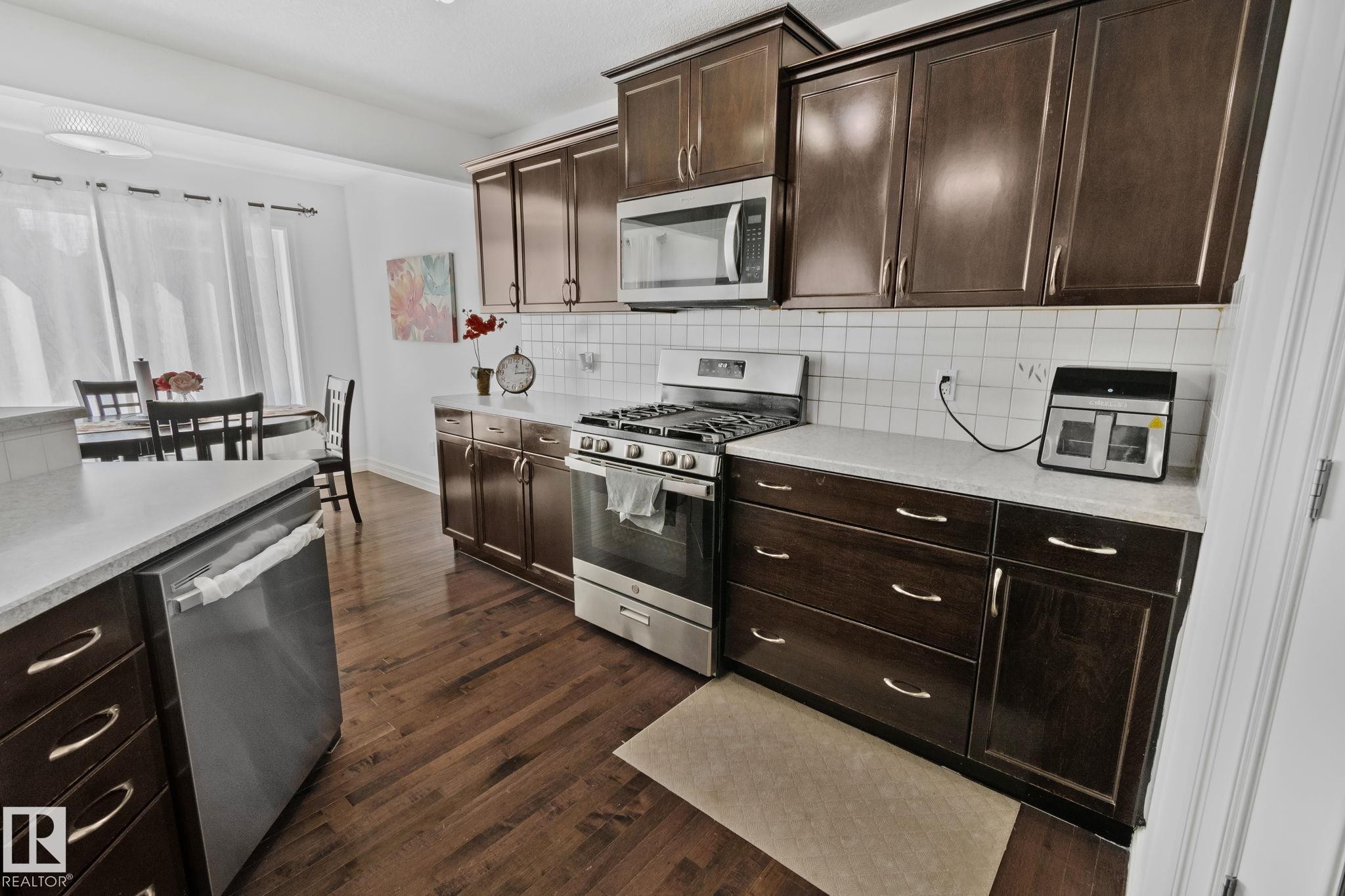The kitchen features dark wood cabinetry, stainless steel appliances, white countertops, and hardwood flooring - 1115 61 Street Sw, Edmonton, AB