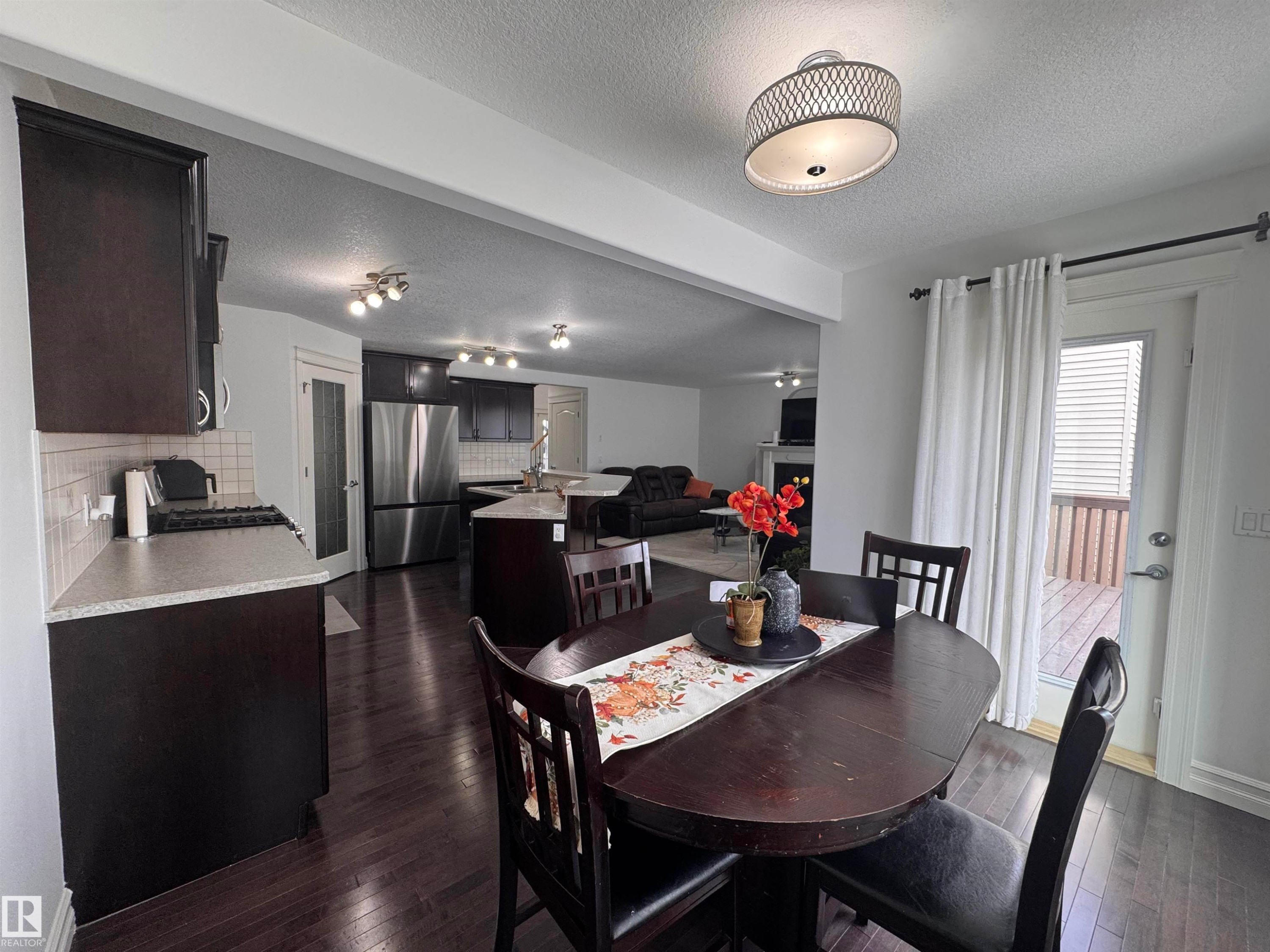 Open concept living space featuring dark hardwood flooring throughout, a kitchen with dark cabinetry and stainless steel appliances, and a dining area - 1115 61 Street Sw, Edmonton, AB