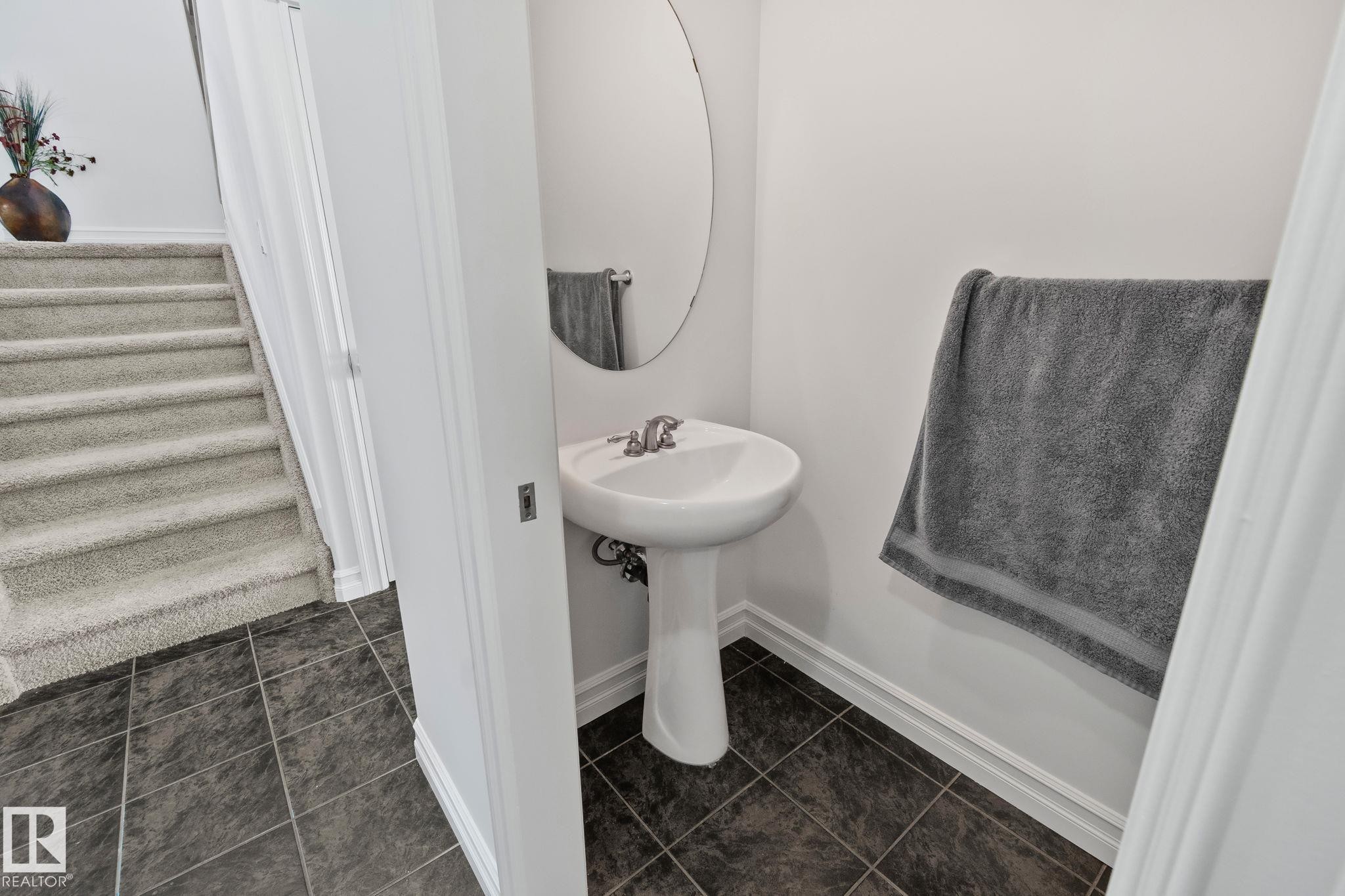 The property features a powder room with a pedestal sink and an oval mirror, complemented by dark tile flooring - 1115 61 Street Sw, Edmonton, AB