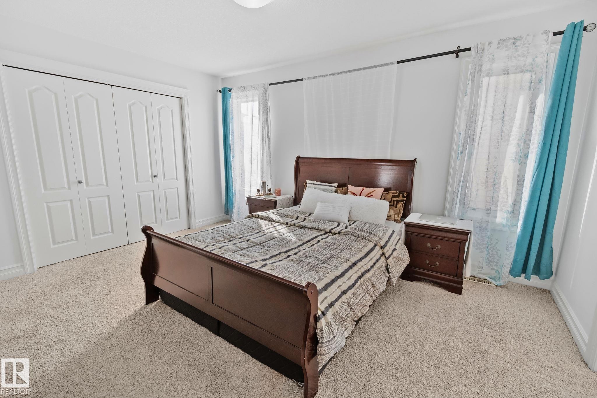 Carpeted room with white walls, featuring a window dressed with sheer and opaque curtains, and a built-in closet with bifold doors - 1115 61 Street Sw, Edmonton, AB