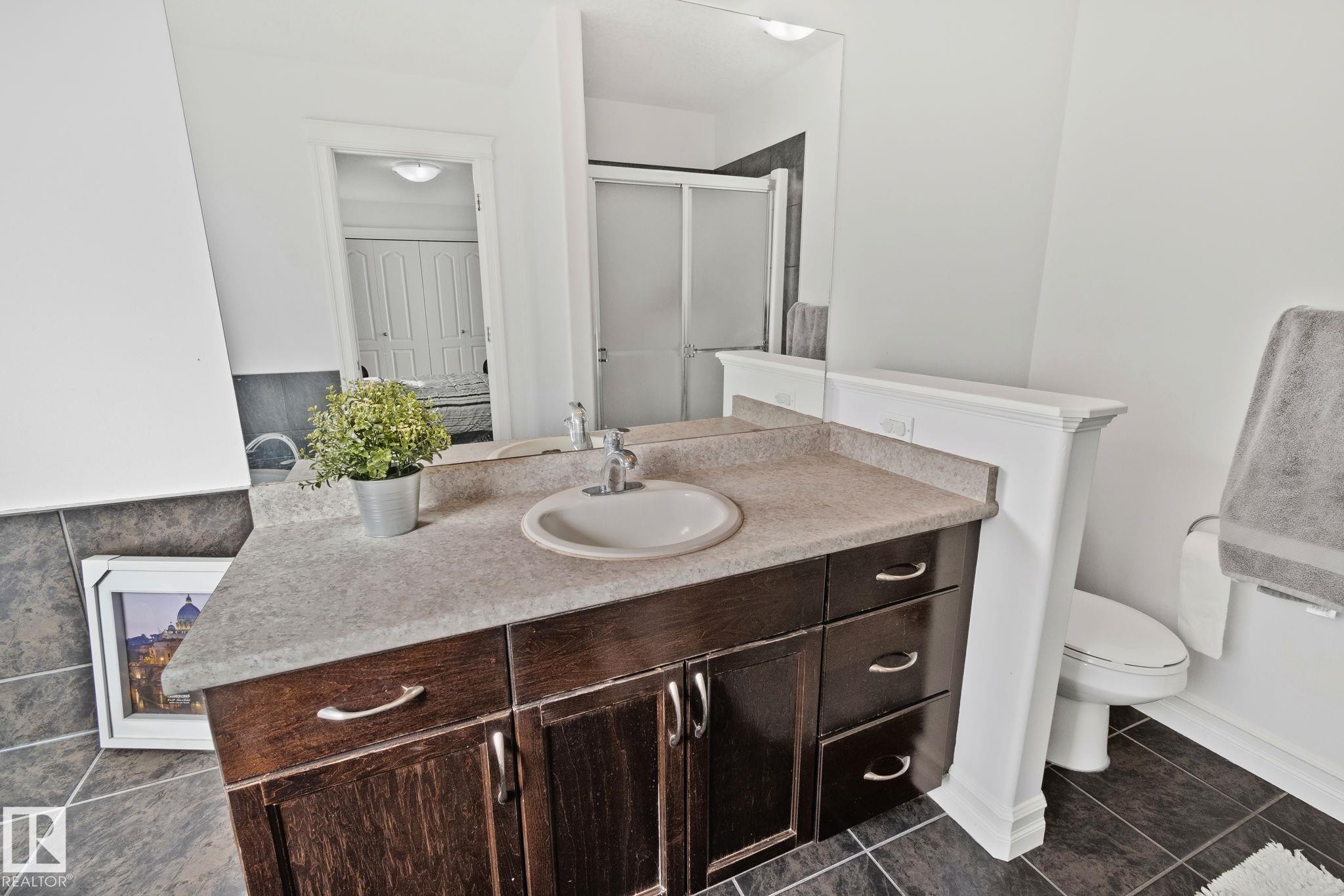 This bathroom features a vanity with a sink, a toilet, and a shower with a clear glass door - 1115 61 Street Sw, Edmonton, AB