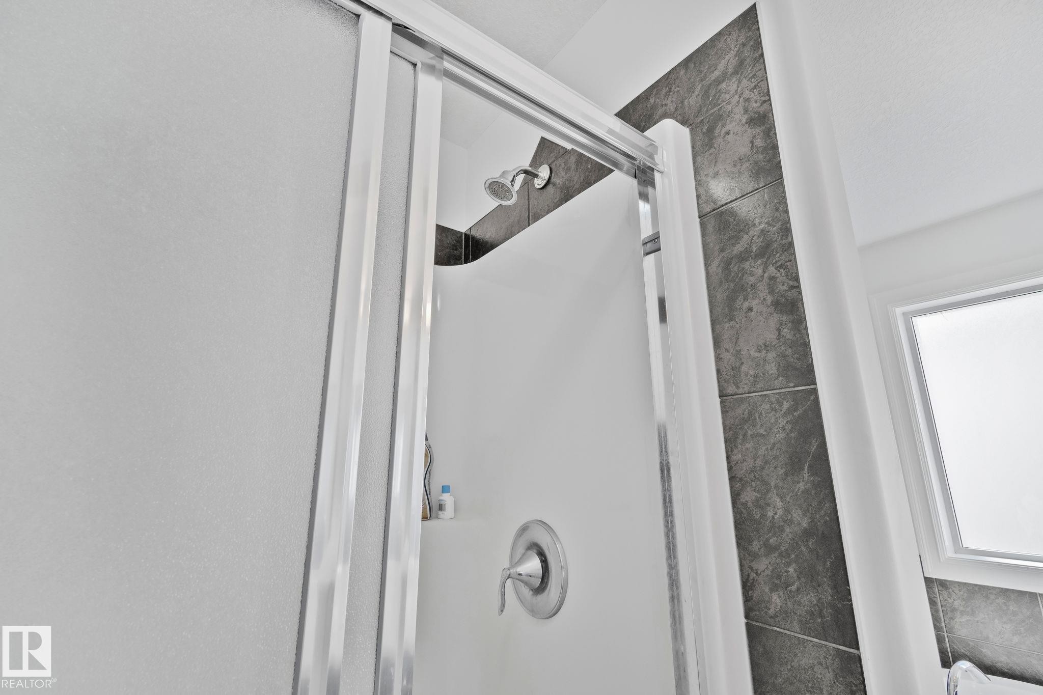 The shower features a sliding glass door, a wall-mounted shower head, and a chrome-finished faucet - 1115 61 Street Sw, Edmonton, AB