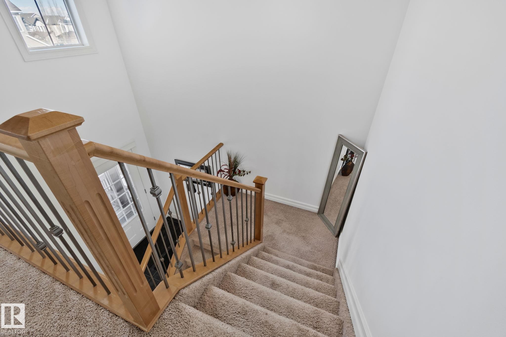 Staircase featuring light wood banisters with dark metal spindles and carpeted treads - 1115 61 Street Sw, Edmonton, AB