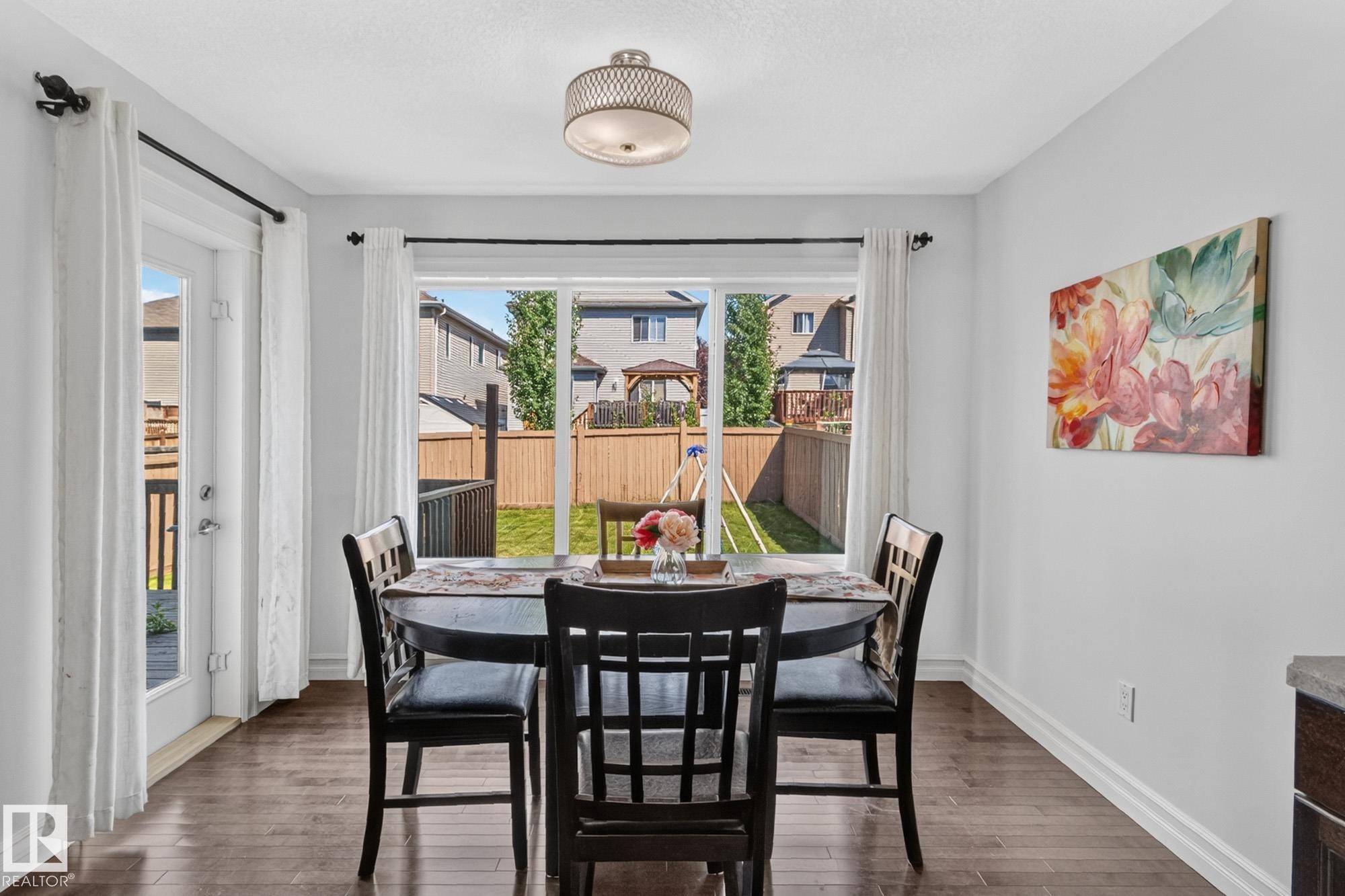 Dining area featuring wood-finish flooring, a contemporary ceiling light fixture, and a sliding glass door providing access to the backyard - 1115 61 Street Sw, Edmonton, AB