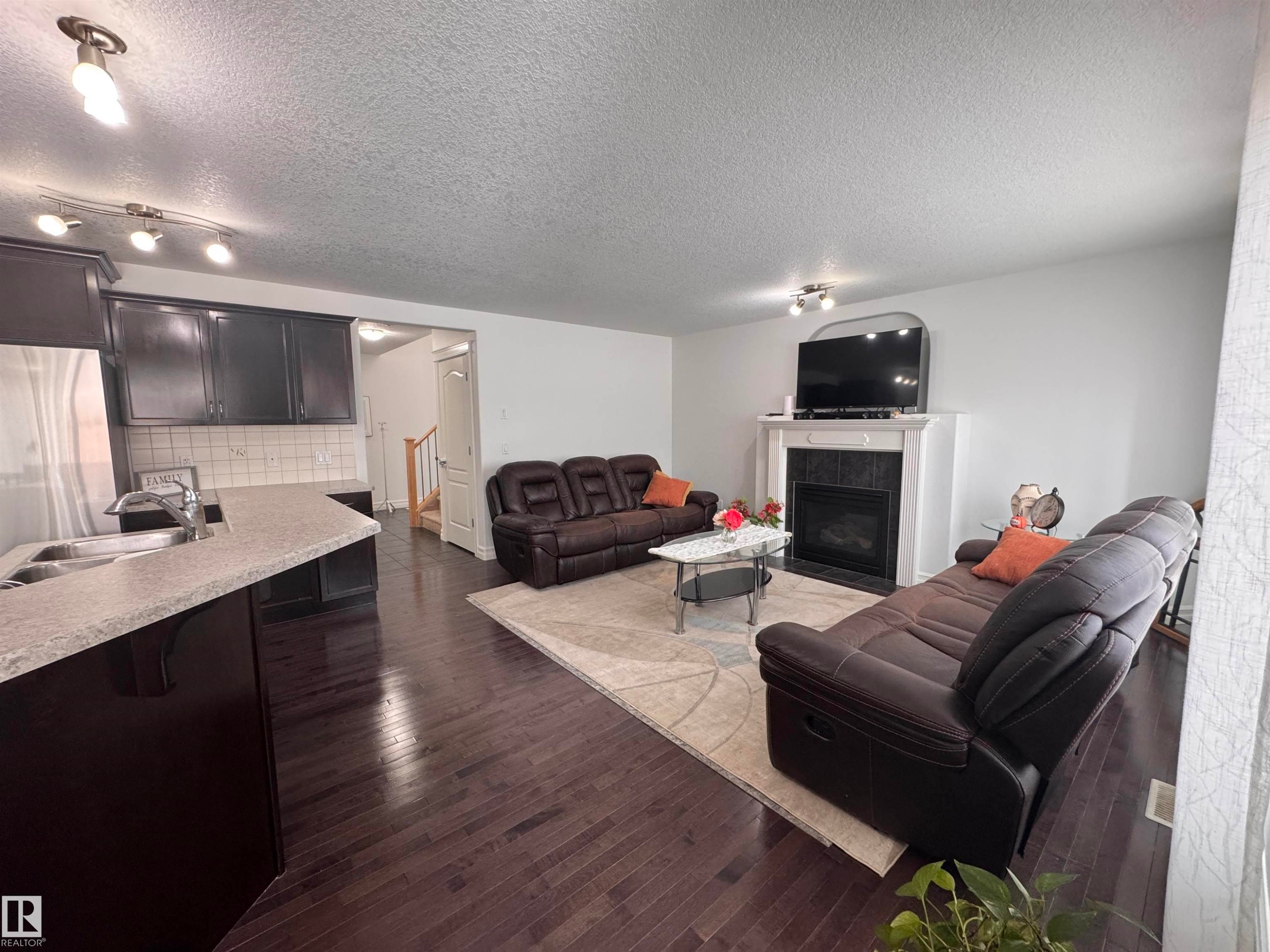 This living space features dark wood flooring, a fireplace with a white mantel, and light-colored walls - 1115 61 Street Sw, Edmonton, AB