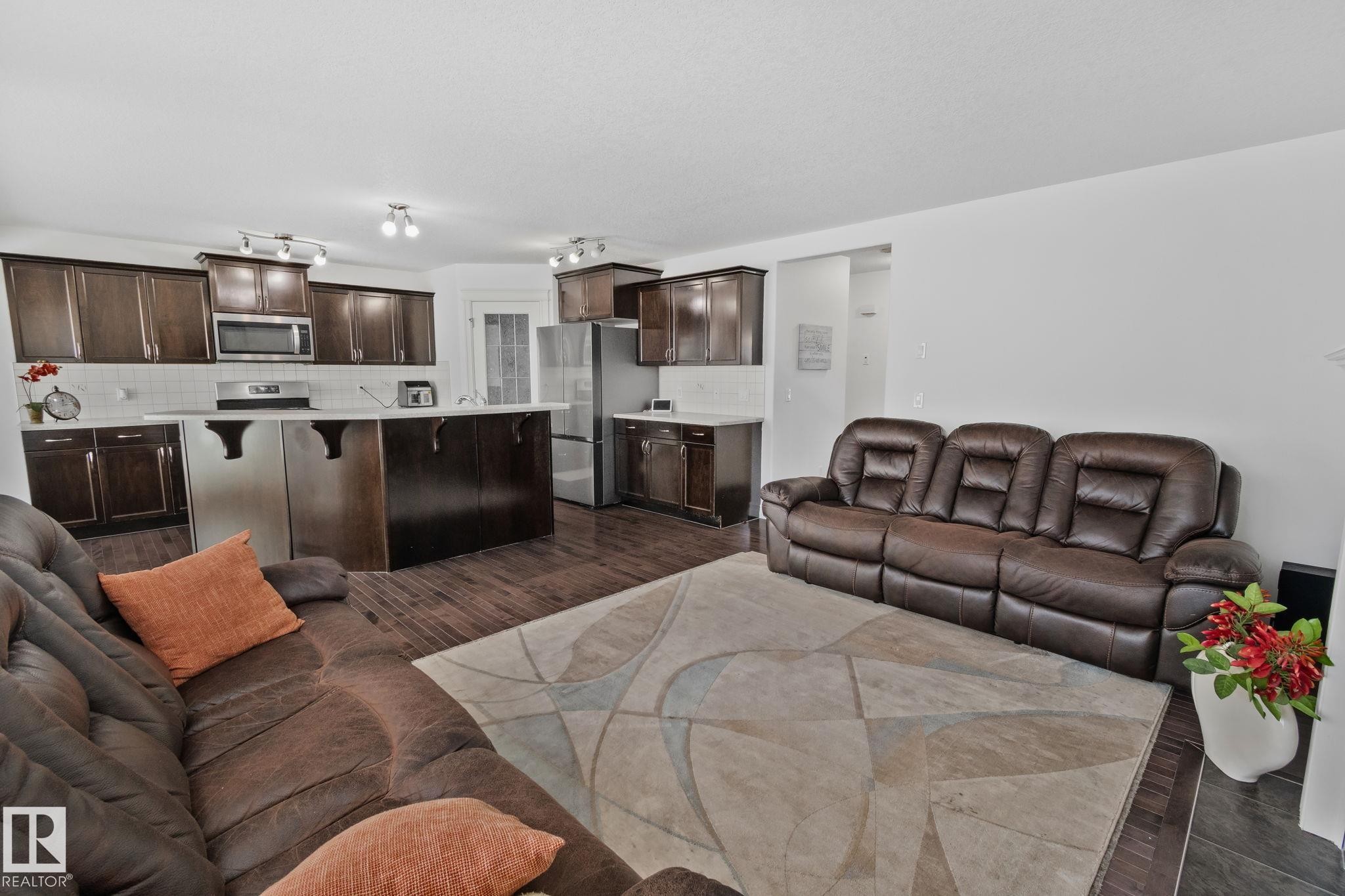 Open concept living area featuring dark wood flooring, an island kitchen with dark cabinetry, and white countertops - 1115 61 Street Sw, Edmonton, AB