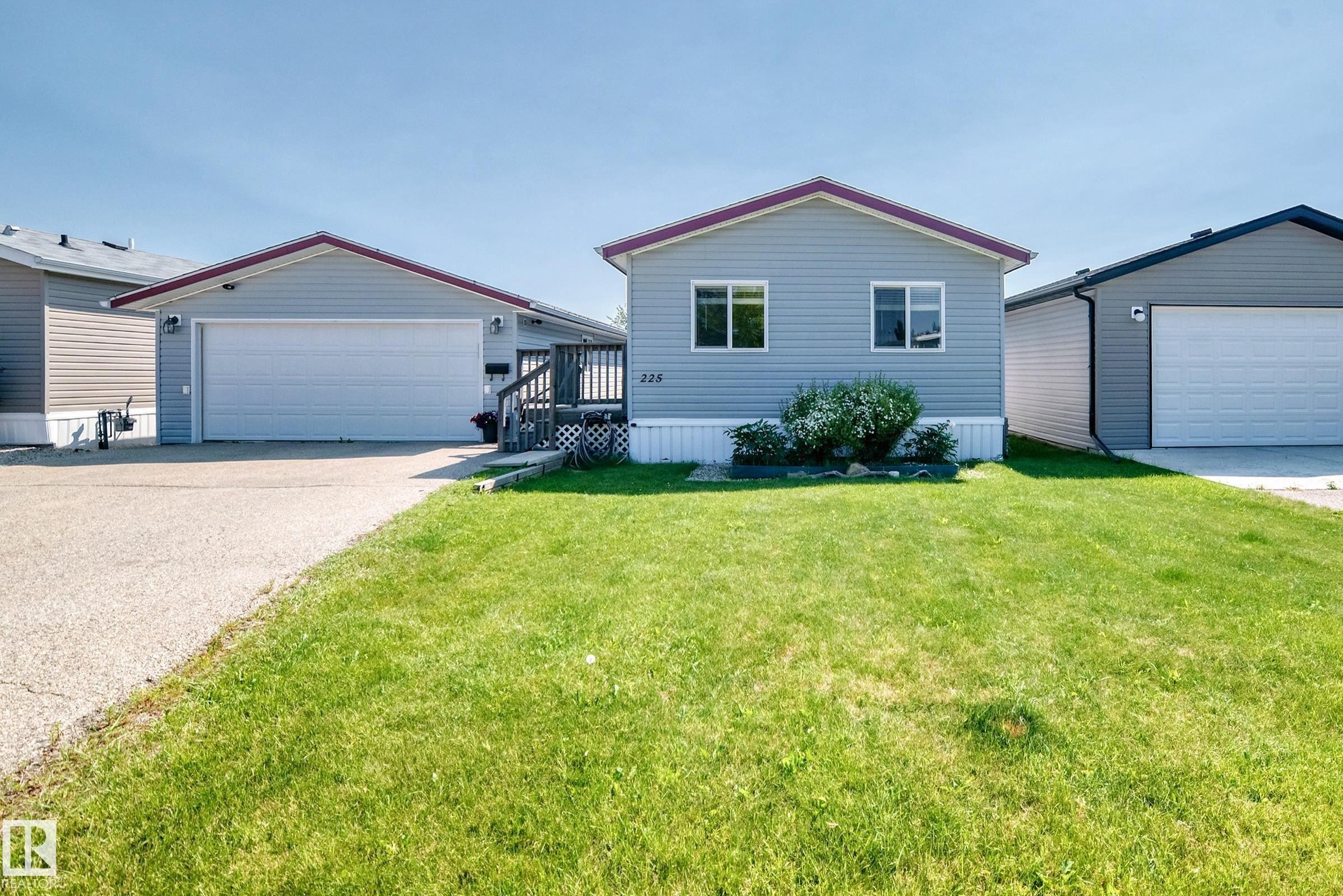 Light gray siding home featuring a front lawn and a wooden deck entry - #225 3400 48 St, Stony Plain, AB - Outdoor With Exterior