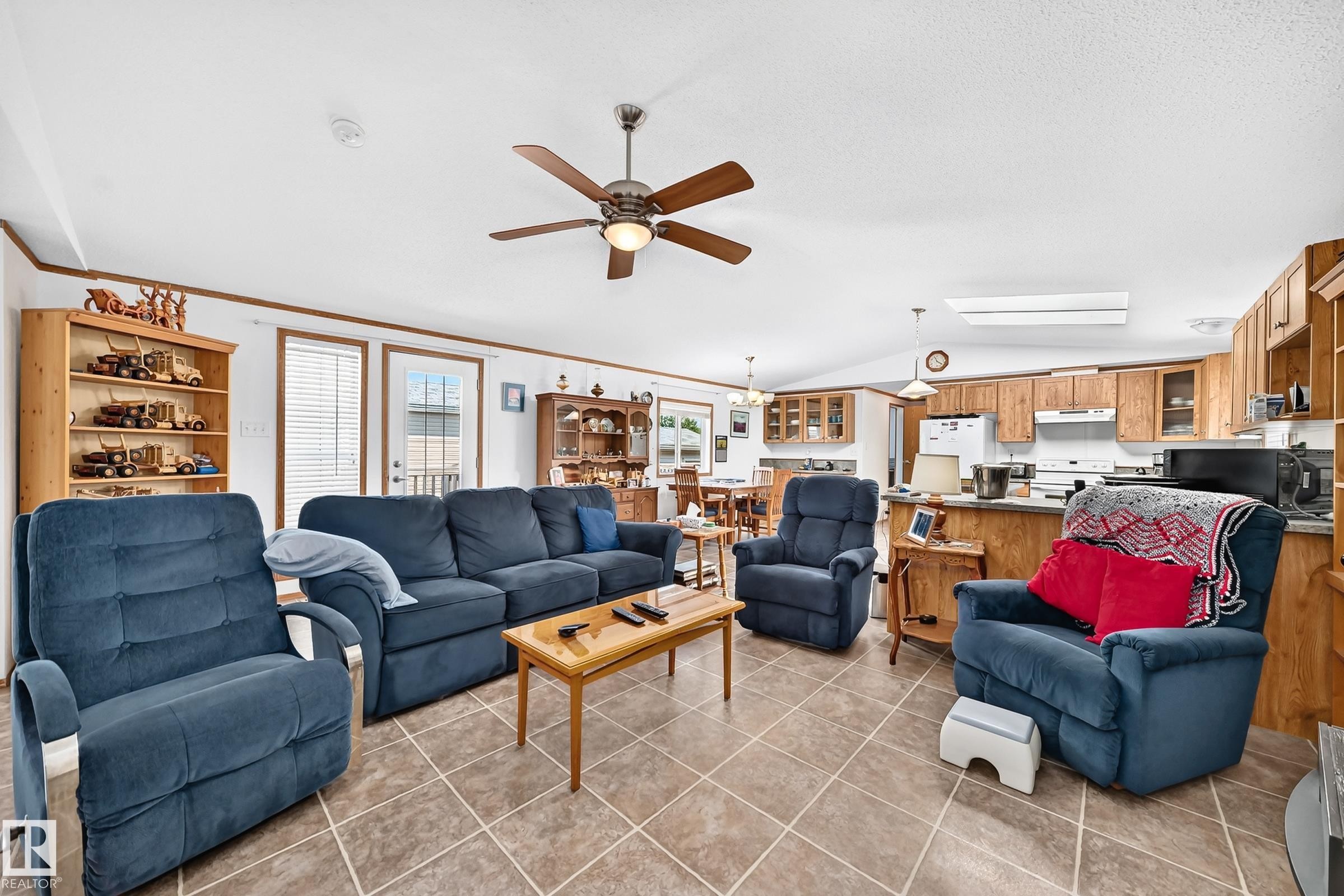Open-concept living area featuring tile flooring, a ceiling fan, and white walls with wood trim - #225 3400 48 St, Stony Plain, AB - Indoor Photo Showing Living Room